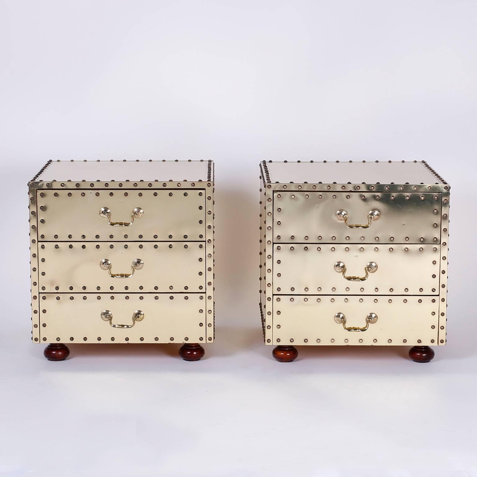 Dashing pair of three-drawer stands or nightstands with an intriguing combination of influences. Having a sleek midcentury form than clad in riveted brass as an Industrial piece yet set on Classic turned wood feet. The result is a creative hybrid of