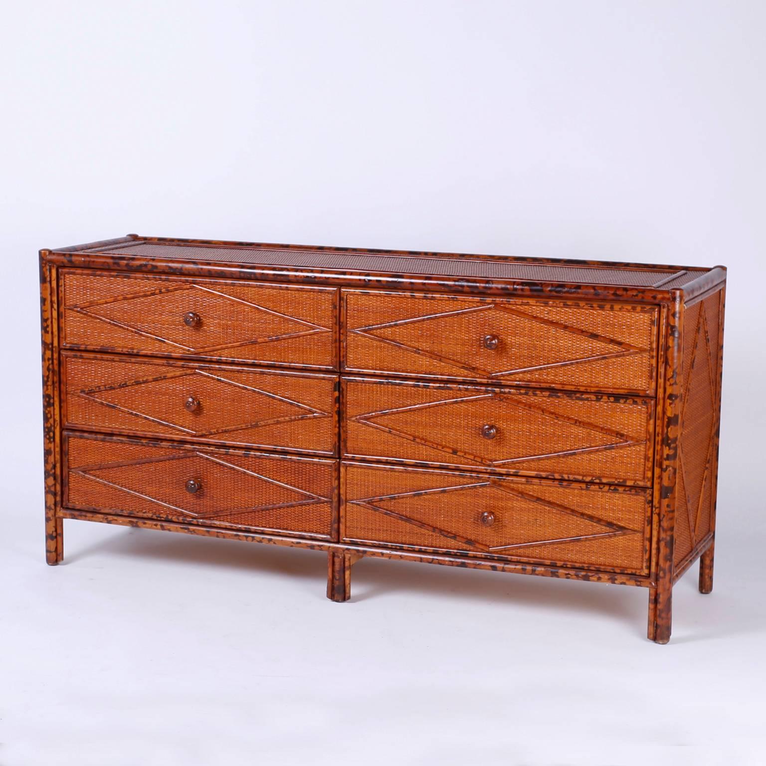 Midcentury British Colonial style burnt bamboo and grass cloth double dresser or chest of drawers with six drawers. The top, sides, and drawer fronts are grass cloth bordered and geometrically decorated with faux burnt bamboo. Sold exclusively at