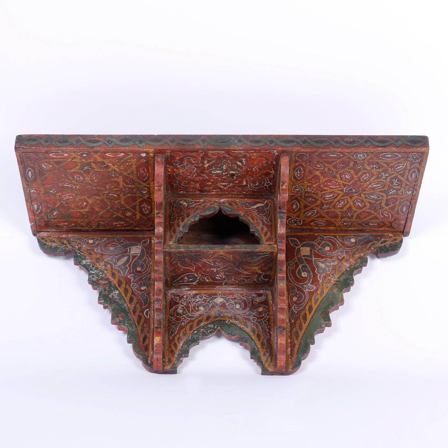 Moroccan wall shelf or British Colonial wall bracket with a gallery around the plateau and an open compartment between two scalloped supports. Painted with traditional folky, rustic colors in symbolic floral and geometric designs.