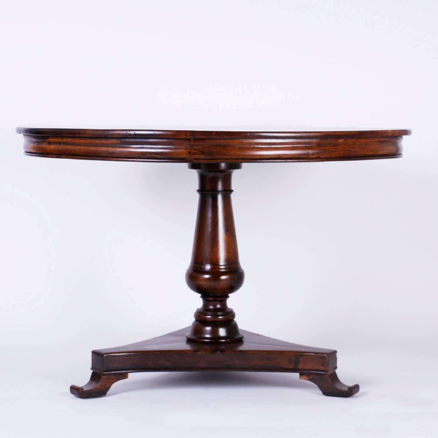 Antique Anglo-Indian dining table or center table crafted with an exotic cut of rosewood, featuring a classical sophisticated casual form with a round top, Bombay skirt, elegant turned pedestal, and a triangular base with sled feet.