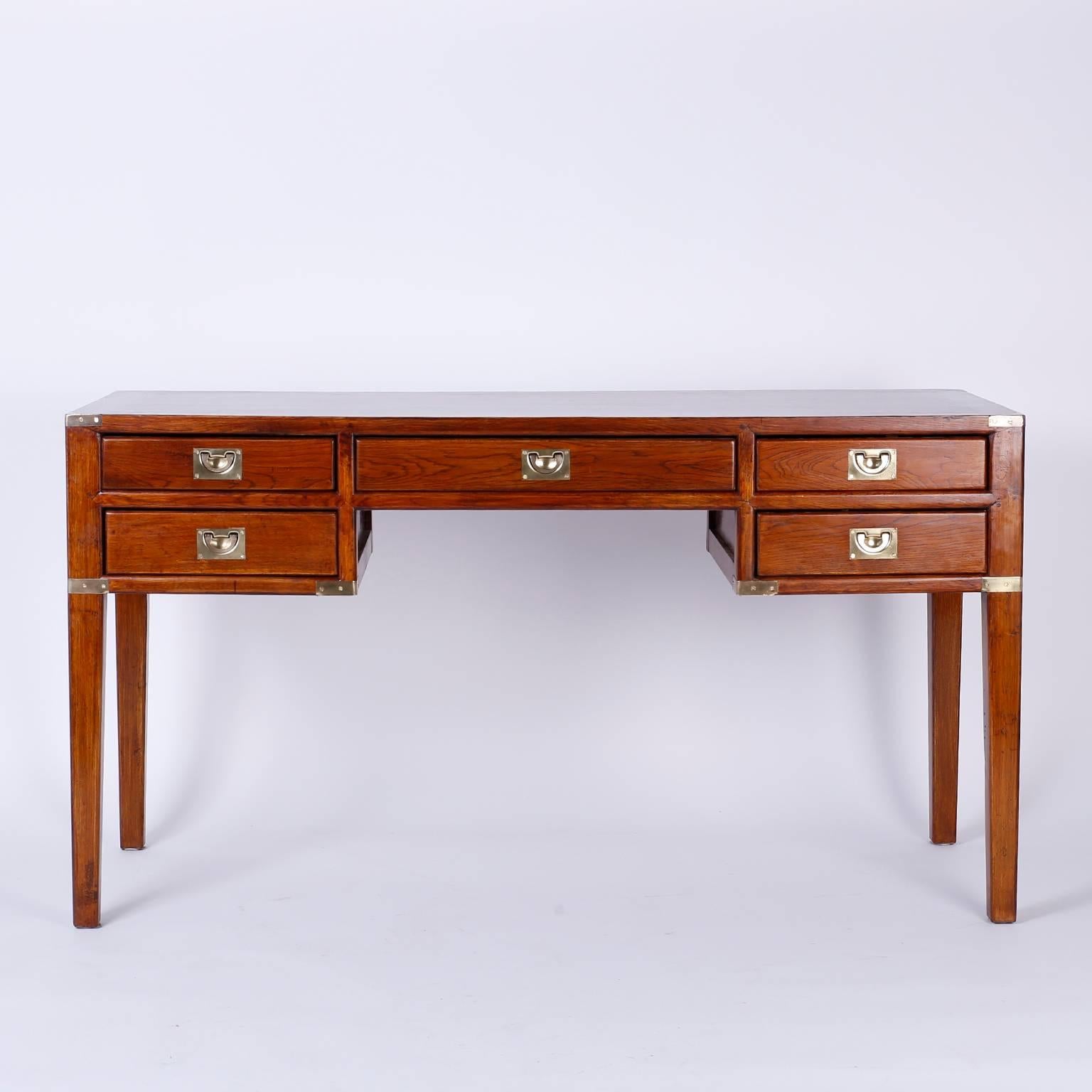 Campaign style desk or writing table with five drawers and polished brass campaign hardware. Crafted in oak with a finished back, tapered legs and sleek clean form that combines tradition with modern.