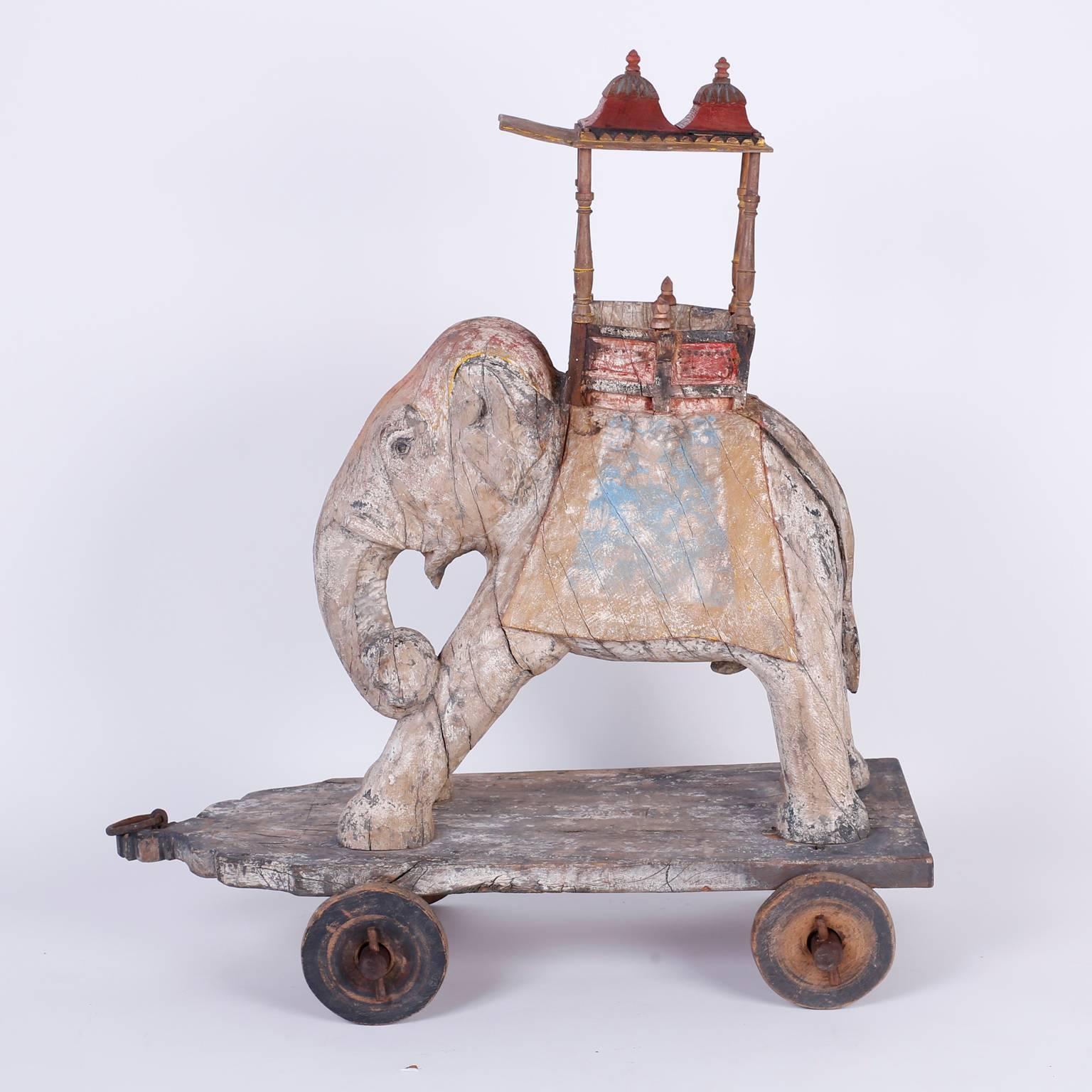 Carved wood antique Anglo-Indian elephant carrying an architecturally interesting howdah and riding on a wood base with wheels. Retaining some of its original paint giving this mobile Pachyderm a charming folky presence, probably a child's toy.