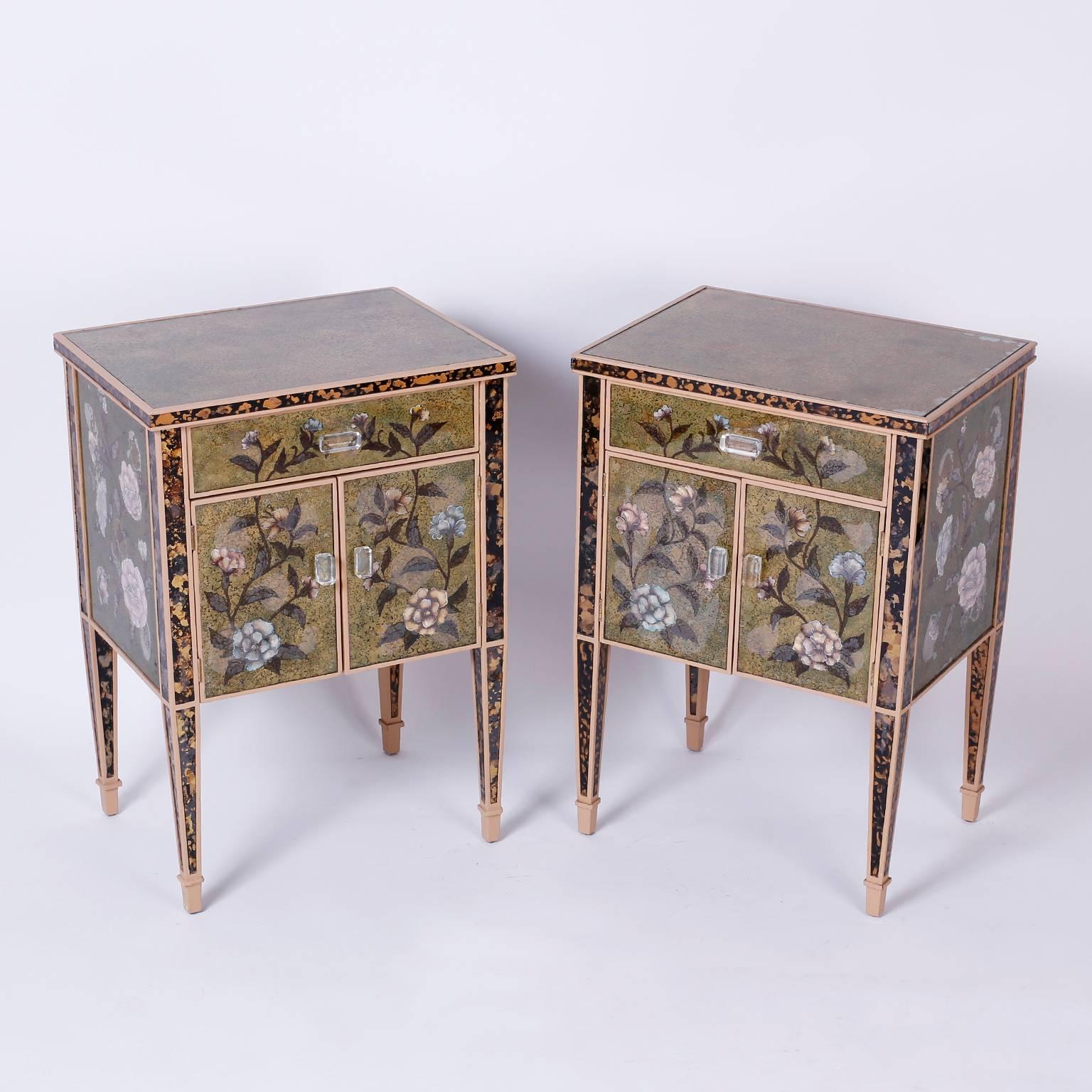 Pair of Italian mirrored nightstands or cabinets with classic form and decorated with chic reverse painted or églomisé floral designs in the Venetian style over a green background. Each with one drawer and two cabinet doors having Lucite pulls.