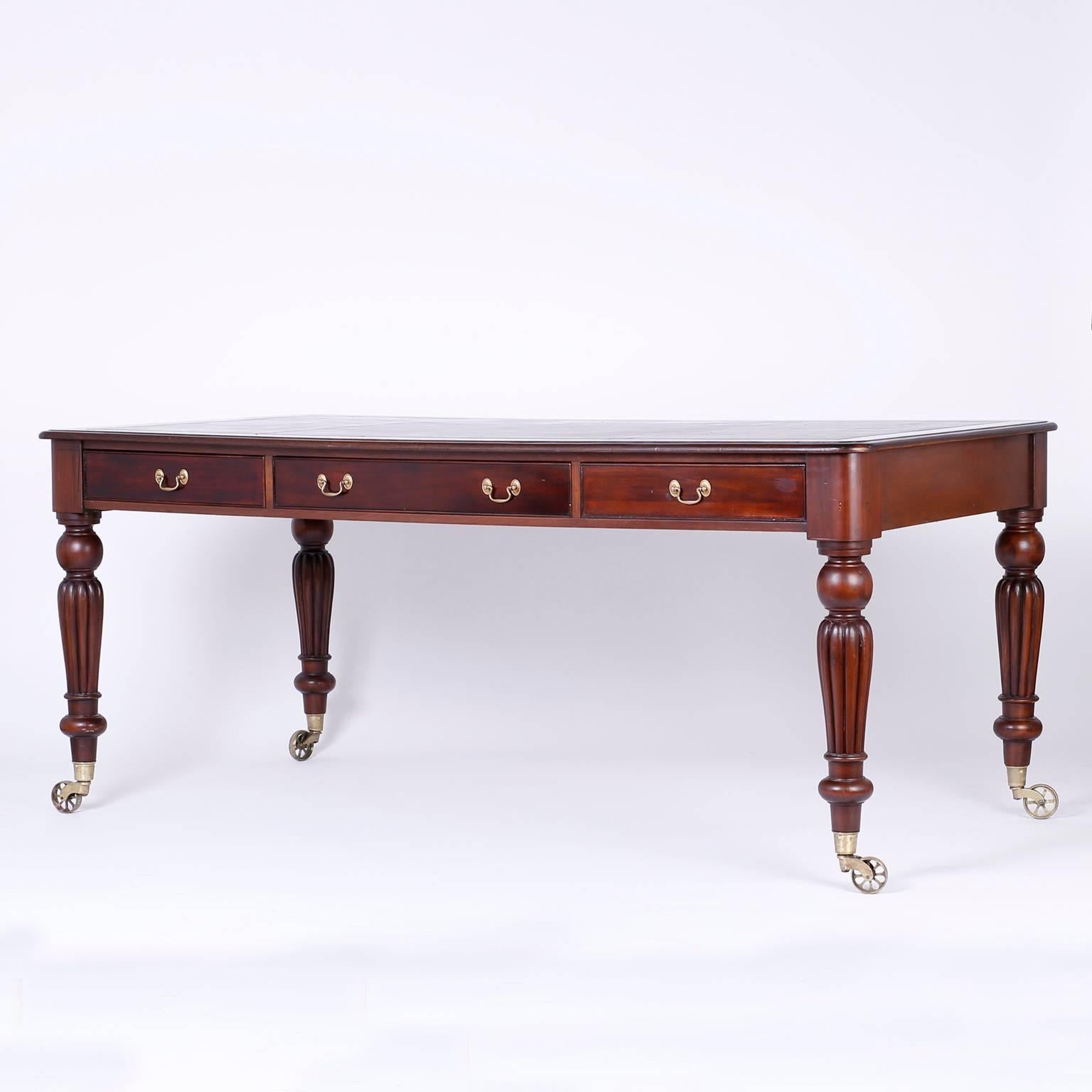 Antique mahogany partners desk or library table in the William IV manner, with a lush tooled brown leather top, three drawers with brass hardware on each side, turned and beaded legs and all-over Industrial style brass wheels. 

             