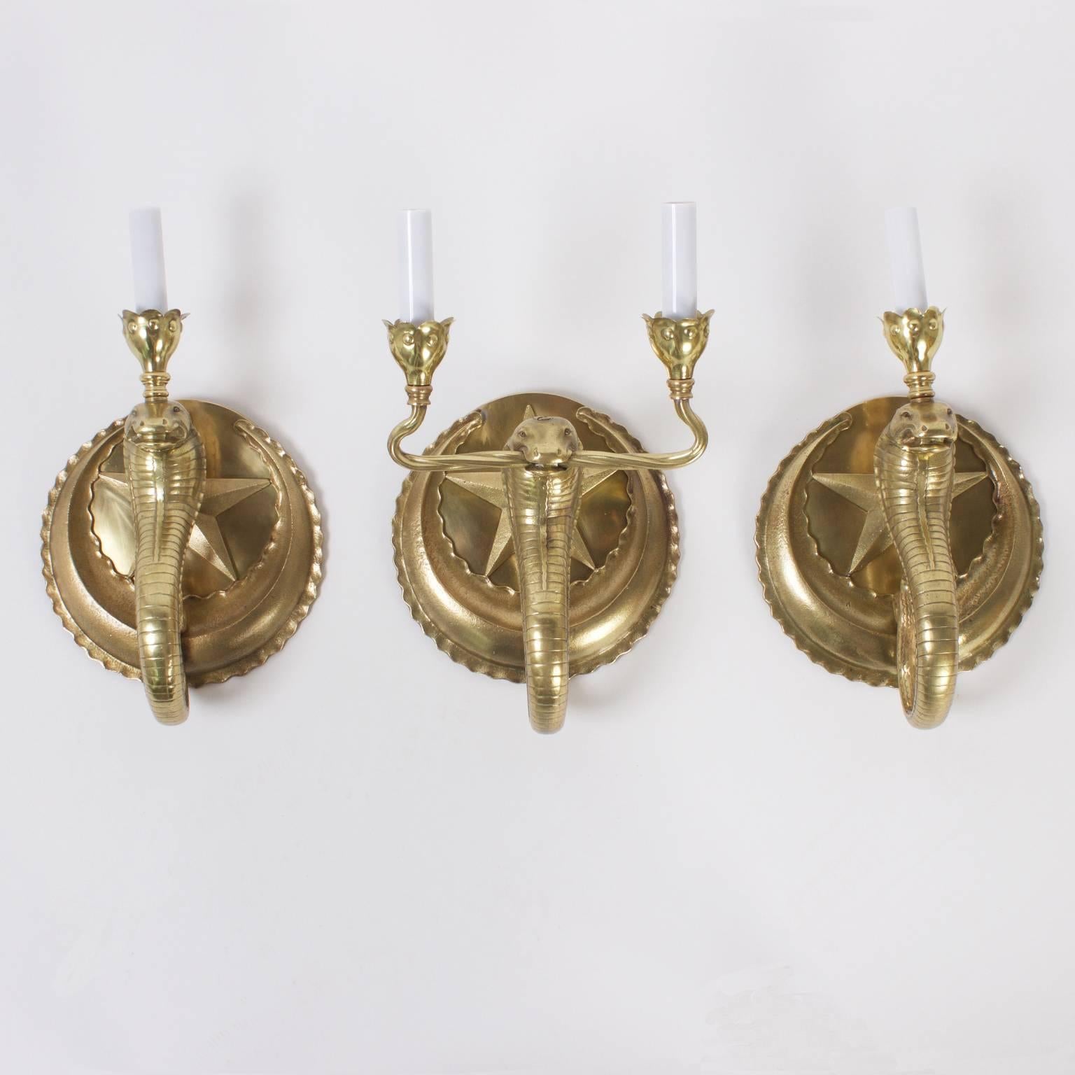 A set of three brass cobra wall sconces, with two single sconces and one double arm sconce. The cobra tails wrap around the sconces for a decorative scalloped effect. Star appliques hide the mechanics of the wiring. Newly wired.

 