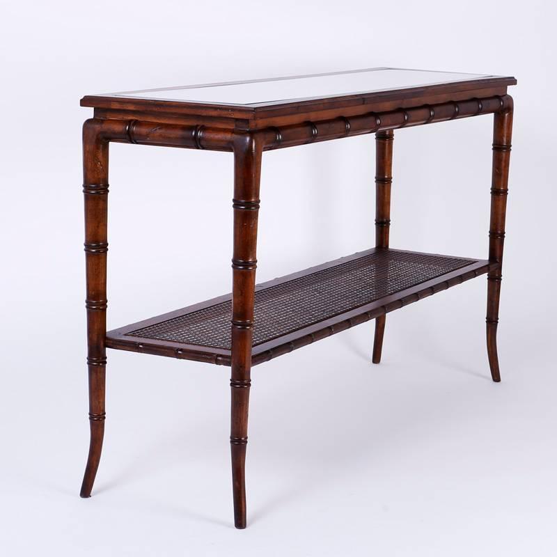 Elegant two-tiered console or sofa table with a carved wood faux bamboo frame and two caned plateaus, the top having inset glass. This vintage console is the perfect combination of quality, style, and scale.