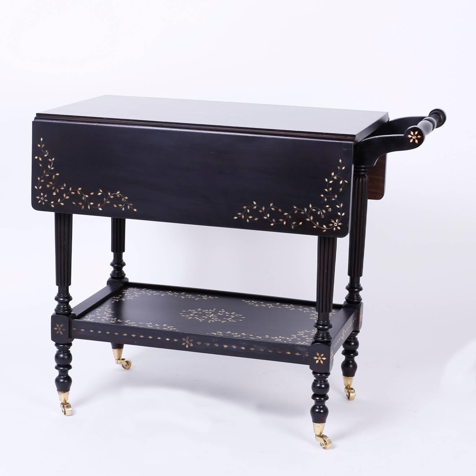 Anglo-Indian hard wood bar, tea or serving cart featuring graceful floral bone inlays, two tiers for service and storage with removable trays, drop leaf top tier, elegant beaded legs, and turned feet on brass casters.