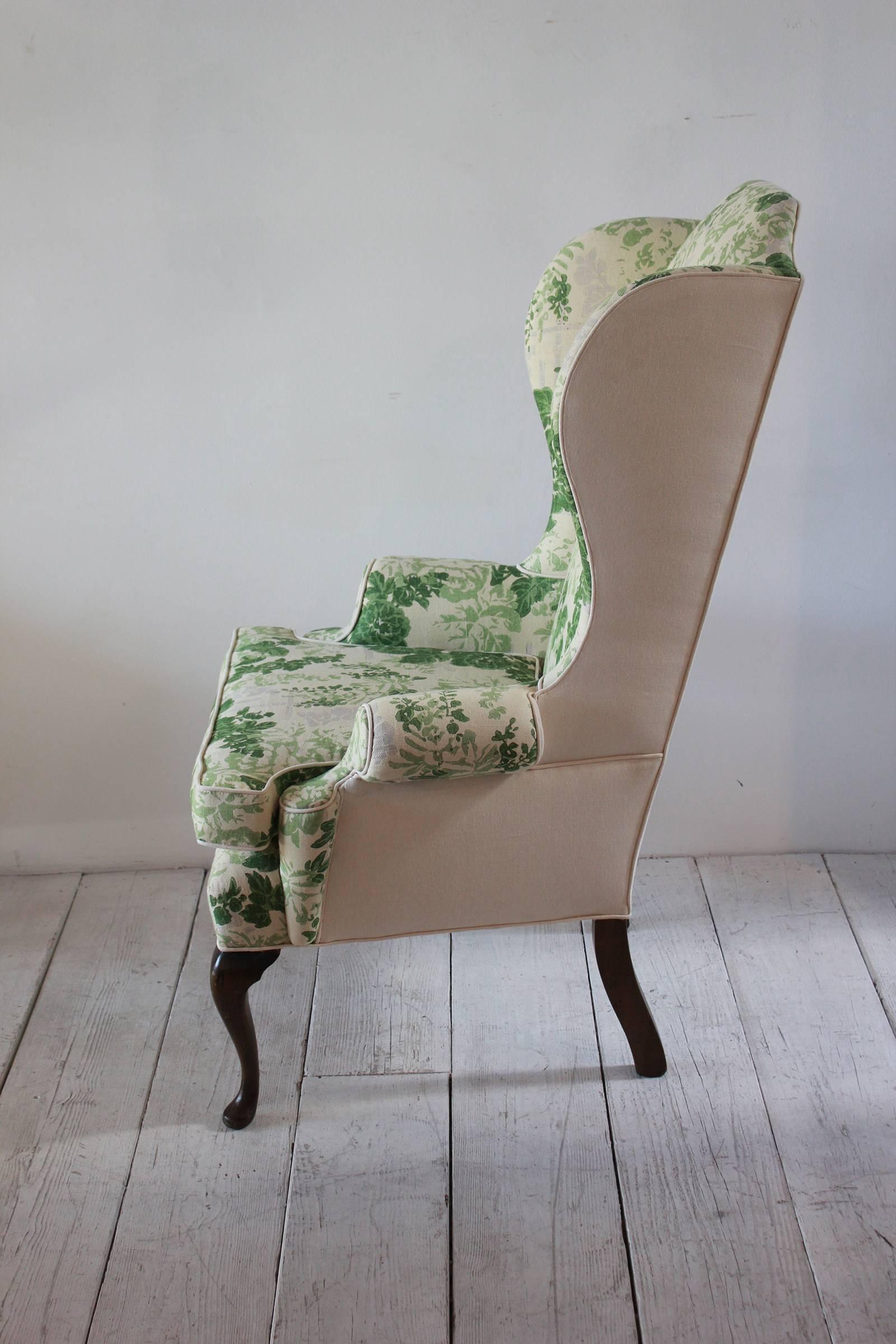 Vintage wing chair upholstered in green floral fabric with dark cabriole legs.
