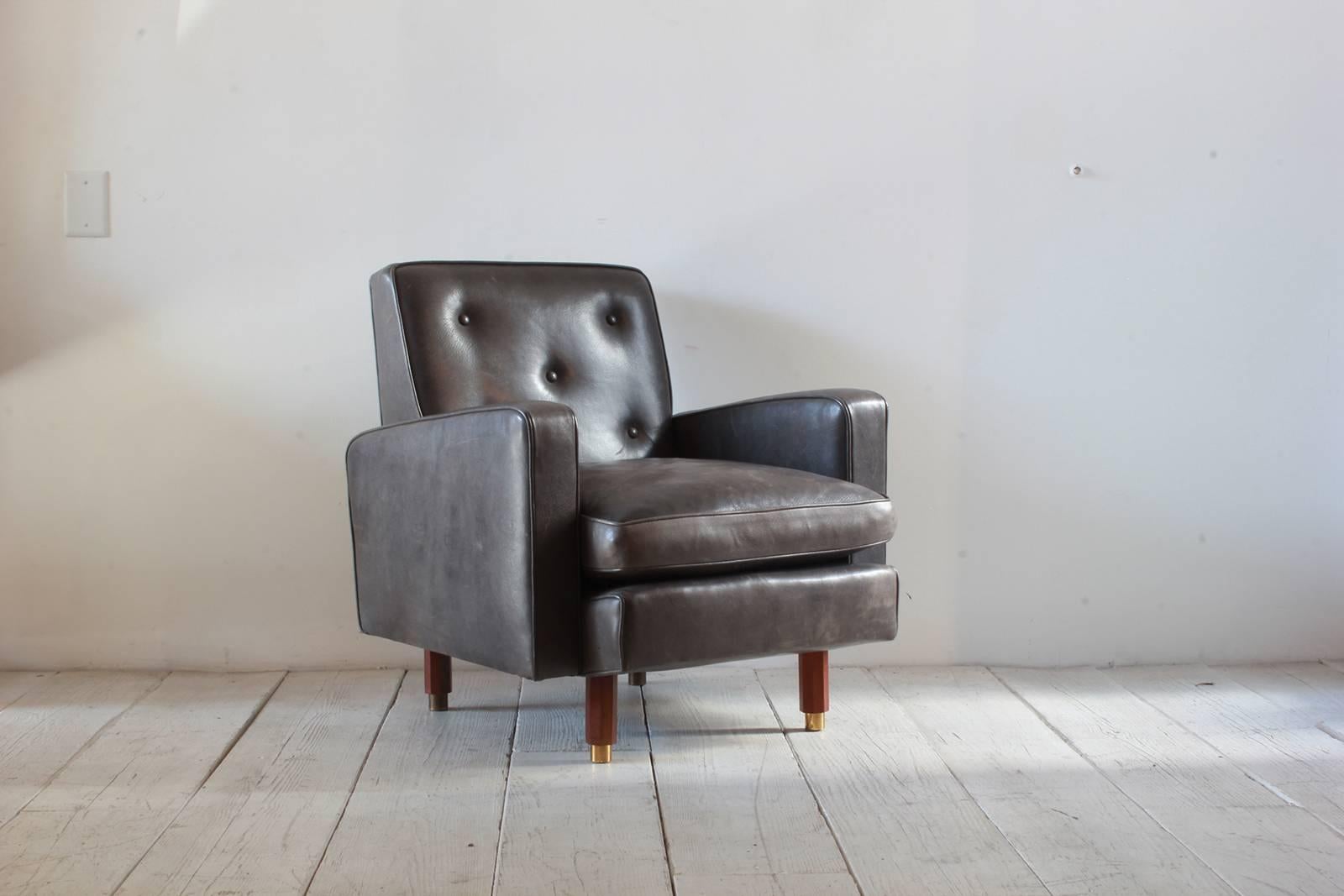 Pair of masculine leather club chairs with five buttons and walnut legs with brass caps.