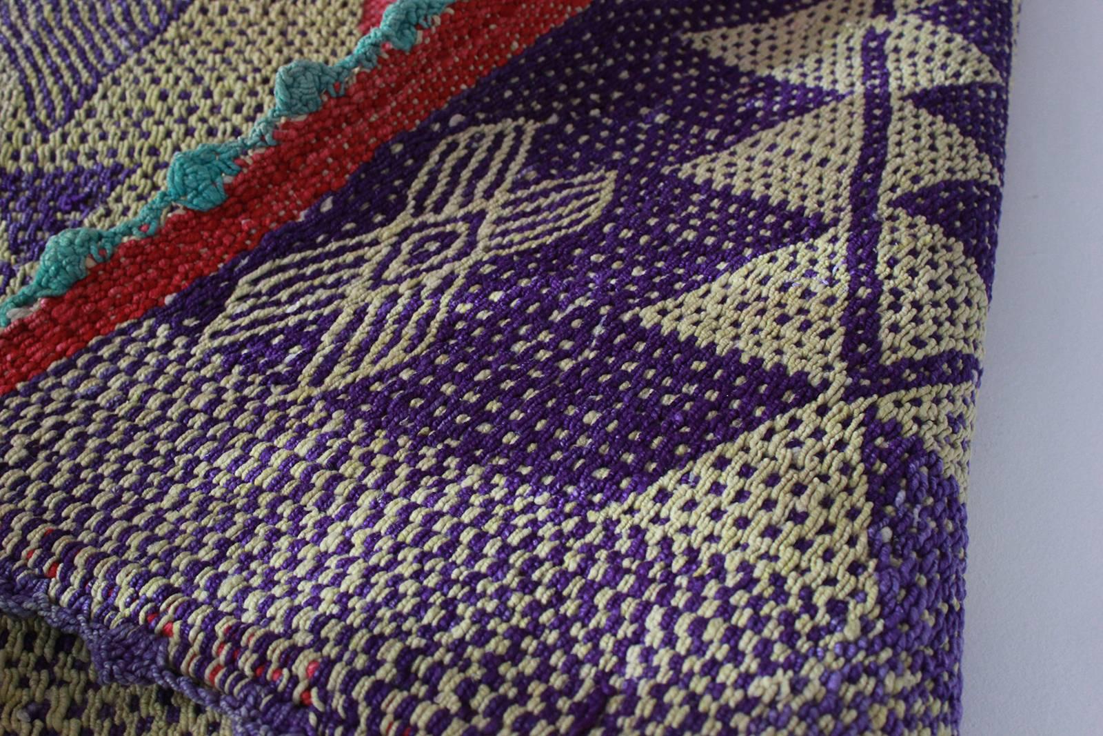 Peruvian handwoven textile with violet geometric details and red border with green accents.