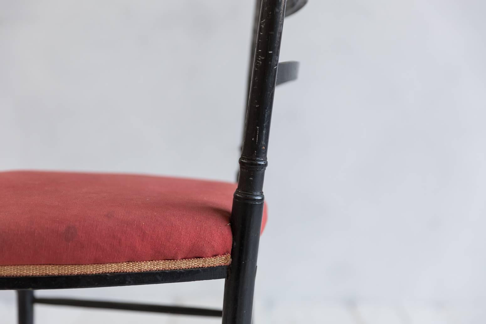 French Chiavari black framed petite side chairs upholstered in original red fabric cushion with delicate trim details.