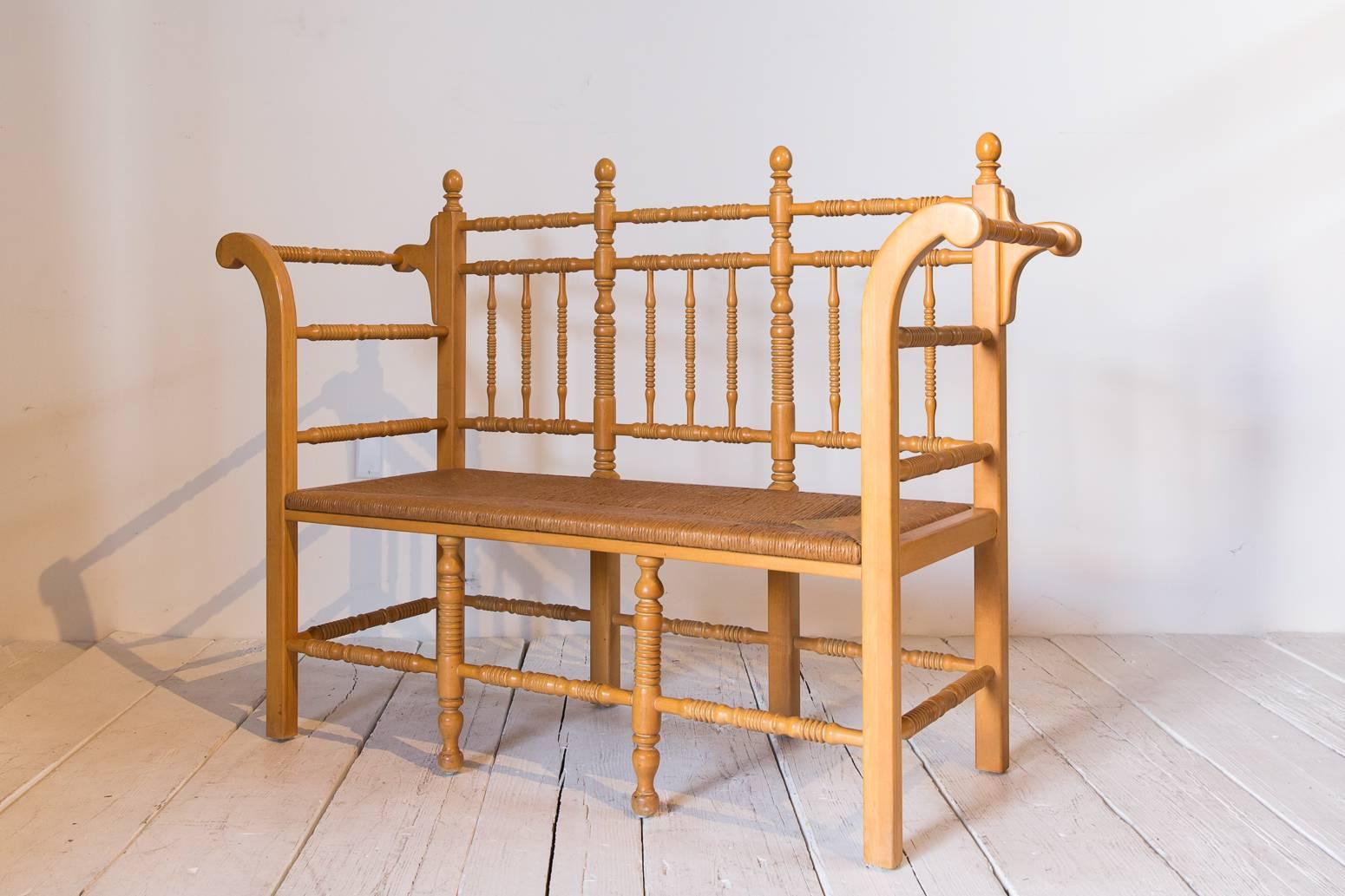 Edwardian style light oak spindle bench with rush seat and curved arms.