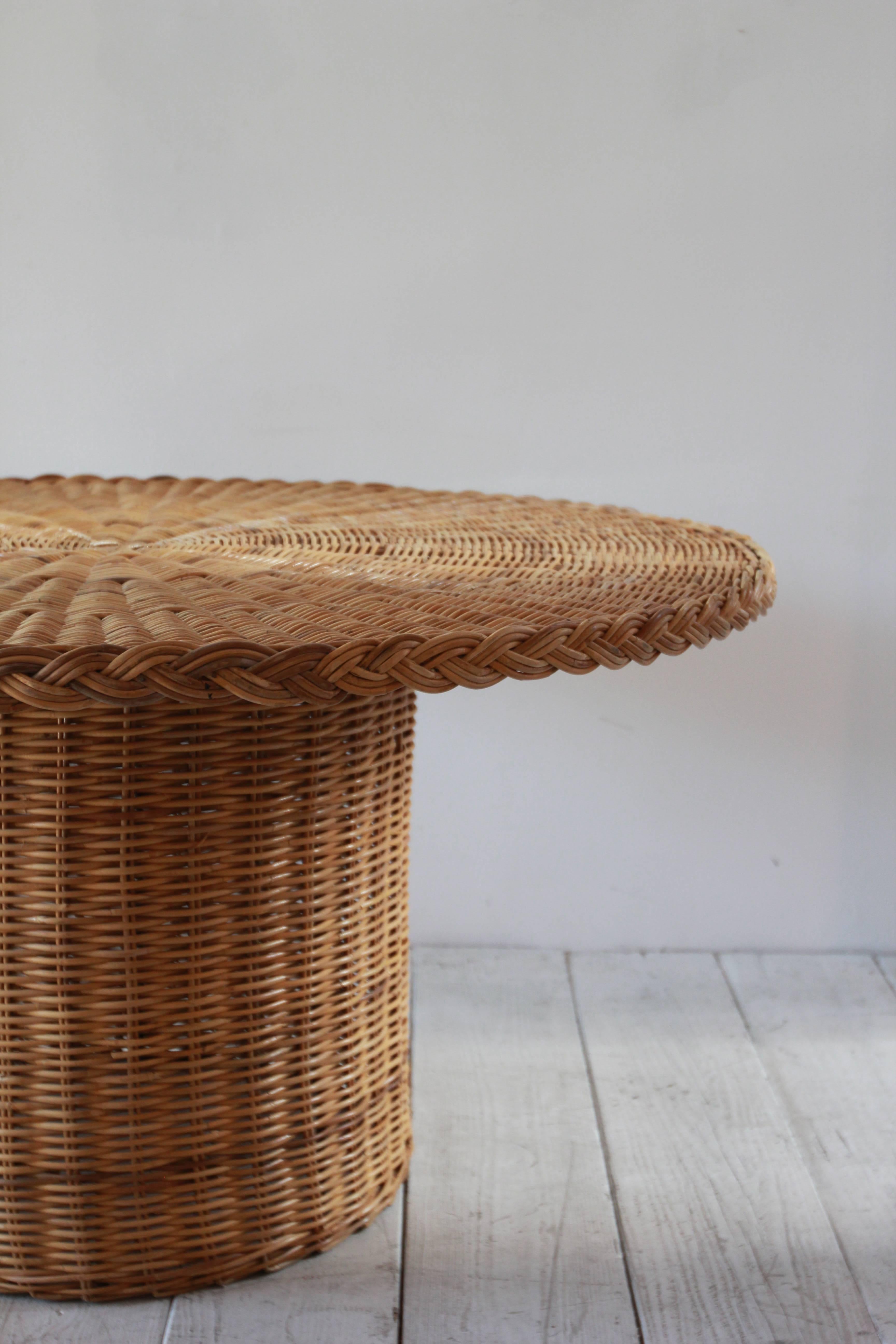 Round rattan dining table with single cylindrical pedestal base.