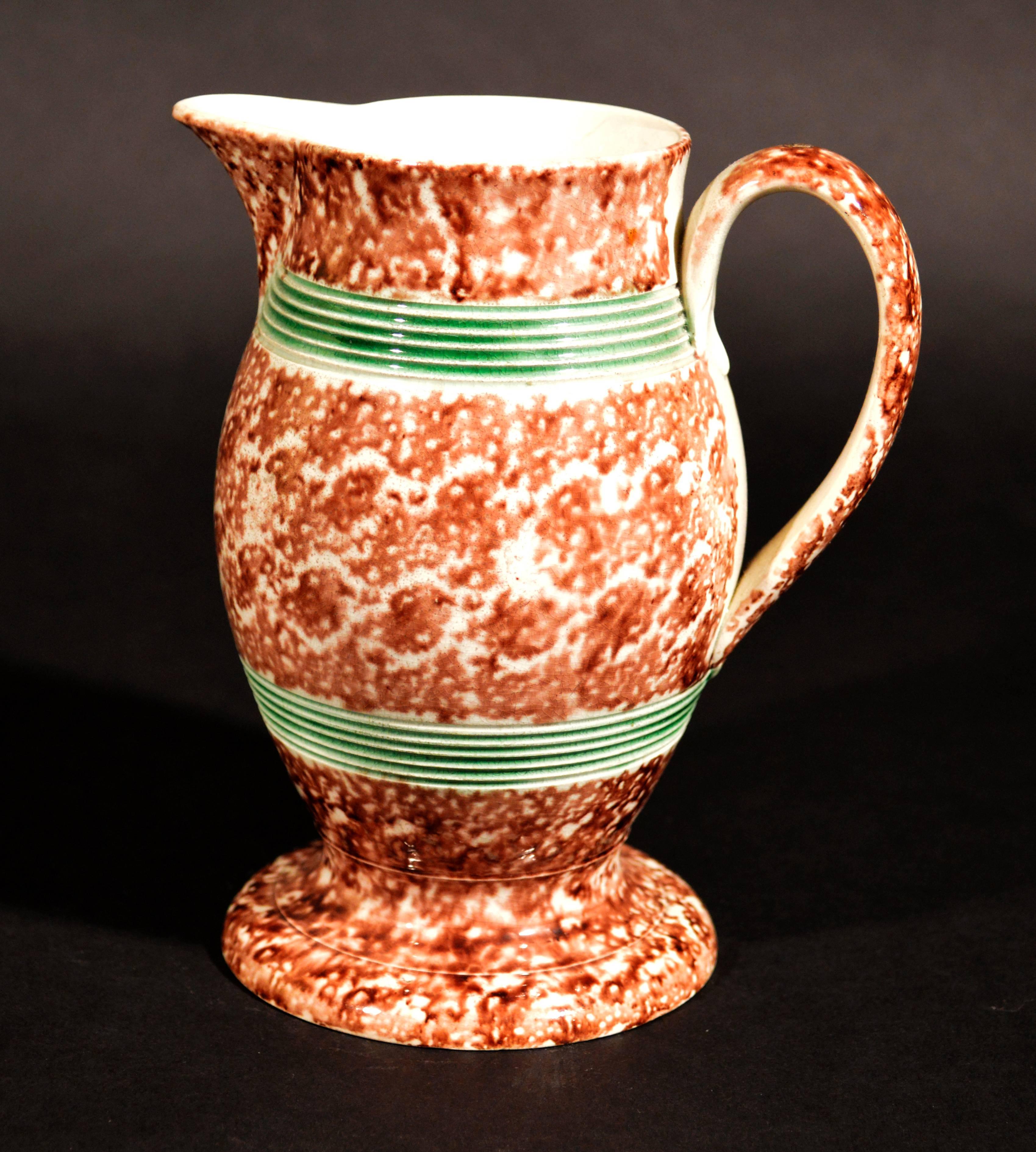 The creamware pottery Whieldon-type jug covered with a tortoiseshell glaze and with two reeded green glazed bands and standing on a splayed foot.

Provenance: Olive Talbot Collection.