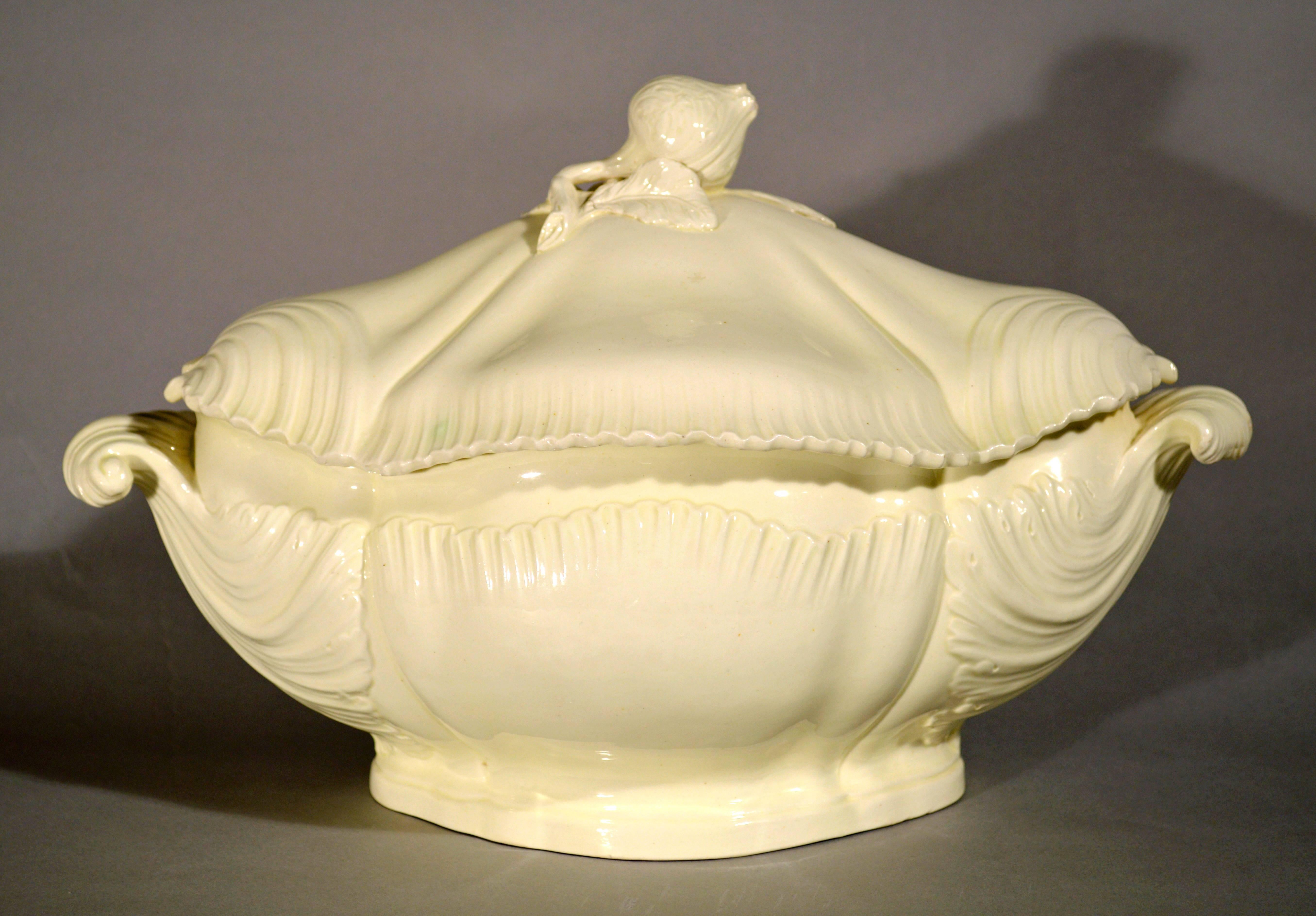 The beautiful plain-creamware tureen is of bombe form and has large scroll shell handles with their moulded terminals swirling almost a quarter of the way back onto the body of the tureen. 

The central section with moulded reeding. The cover is