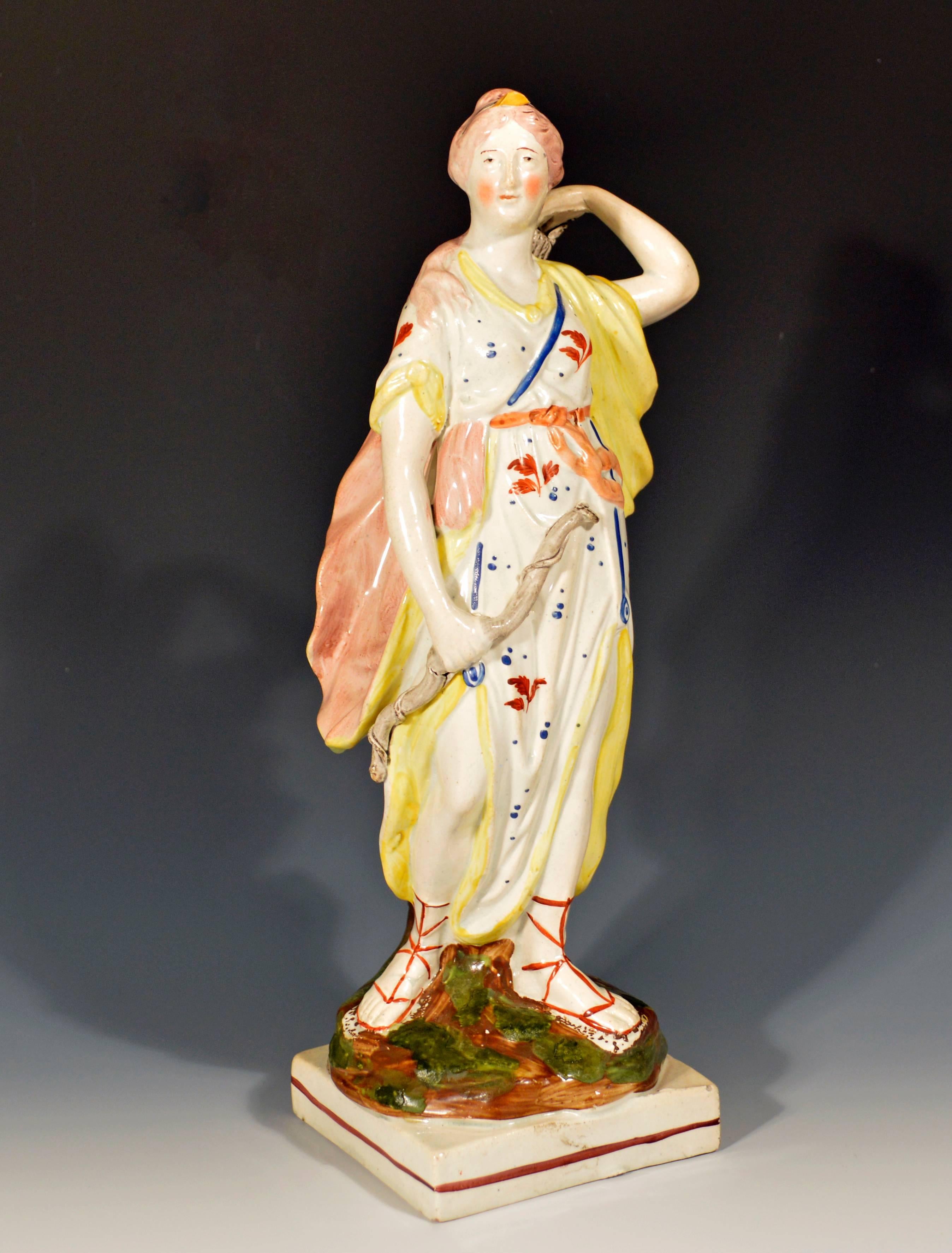 The Staffordshire pearlware figure is either made by Ralph Wood Jr.. or Enoch Wood. The figure with overglaze enamel decoration of orange flowers and blue dots on her dress, all on a hollow square base with a single red-brown line around.

In