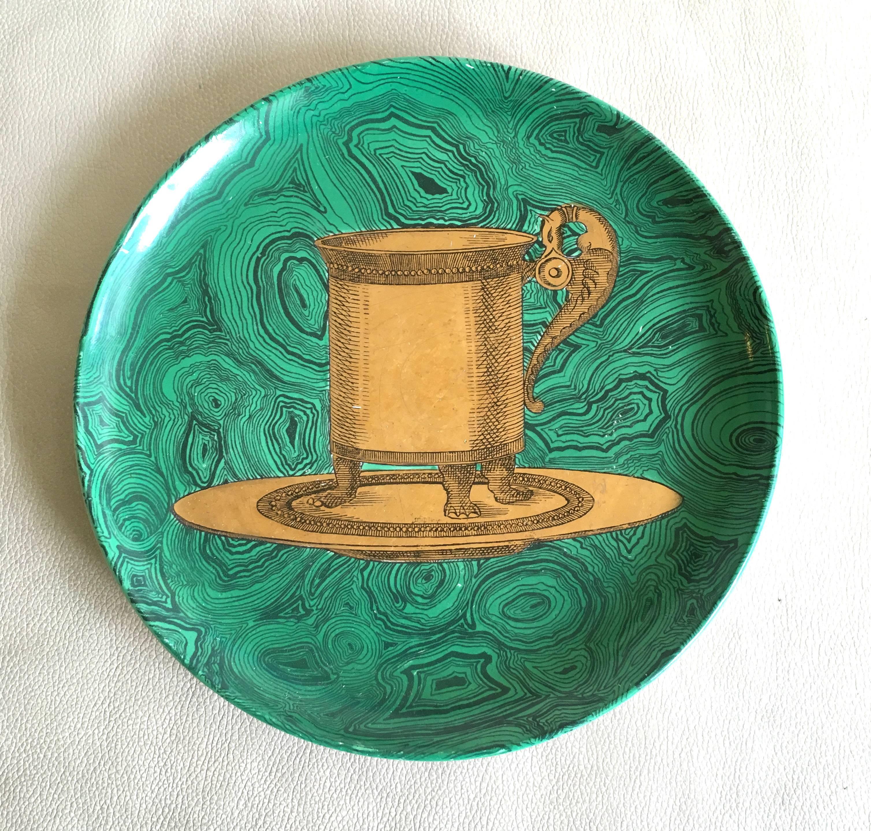 The circular Stoviglie pattern plates by Piero Fornasetti are eary examples from the 1950's.

 The plates are each painted in gilt with a different painting of table accessories on a malachite ground 

The subjects are a water jug (#8), A soup