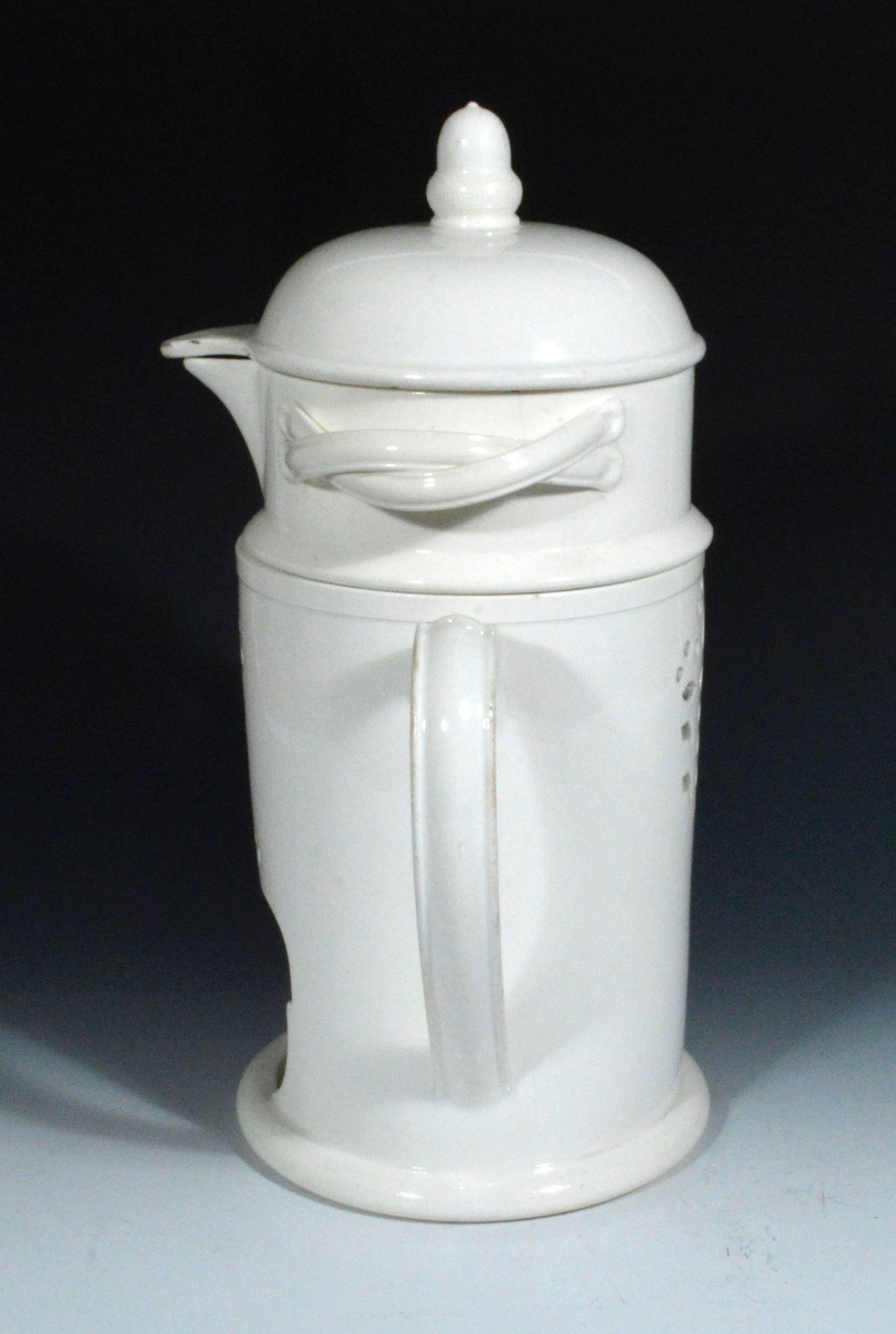 The plain creamware veilleuse consists of three parts- a tall cylindrical base with openwork design of a flowering leaf to front and back and a covered double-loop handled bowl with acorn finial.

An identical food warmer is in Homewood House