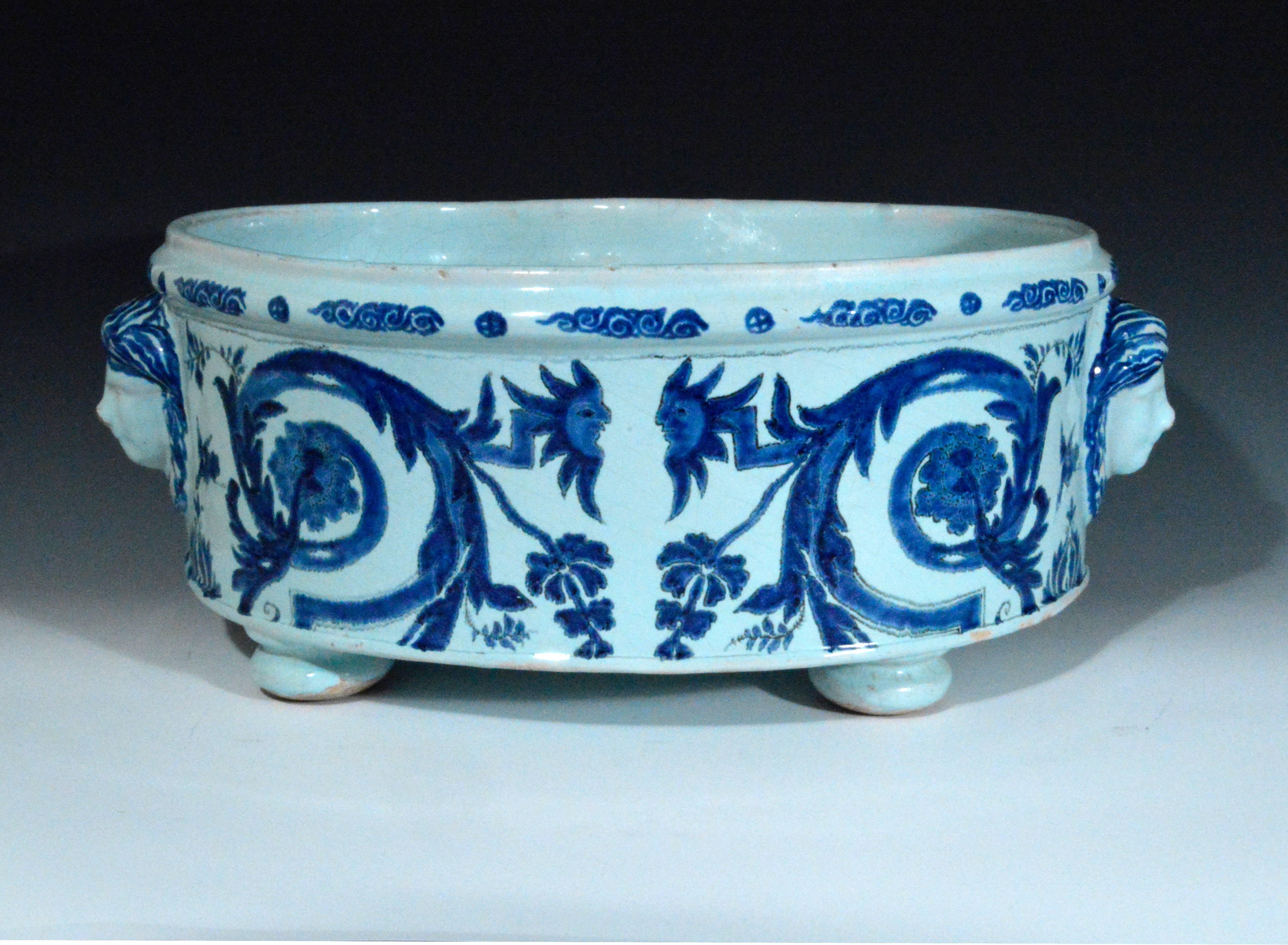 The Lille faience or tin-glazed earthenware under-glaze blue and white heart-shaped basin is supported on three bun feet. The exterior is painted with stylized floral scrolls terminating in sunflower-like flowerheads looking like masks. To each side