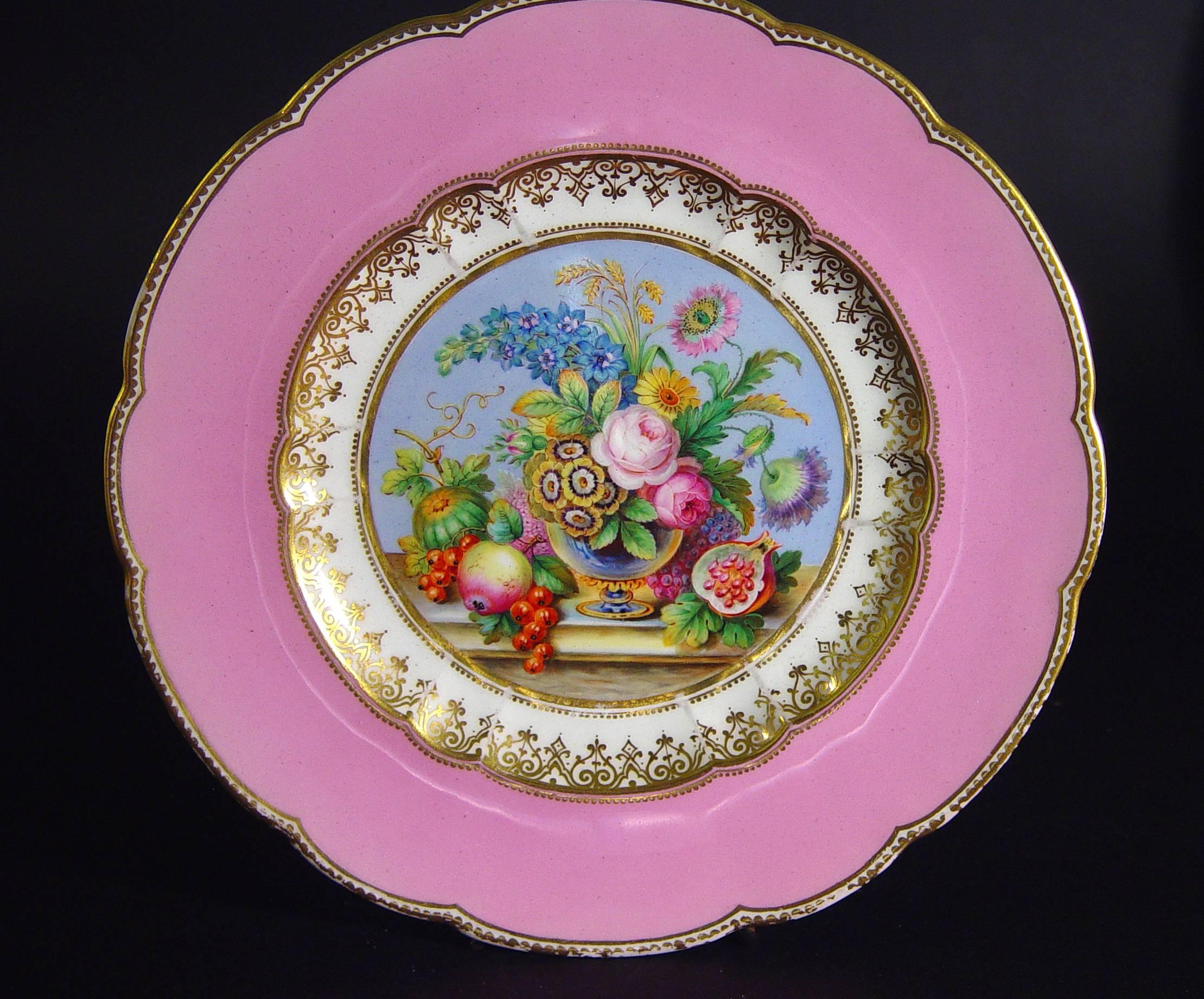 The plates are most likely Minton with very finely painted interior wells of a still life of flowers in urns on a marble tabletop with exotic fruits to either side within a circular gilt enhanced border. The rim with a wide band of pink-ground