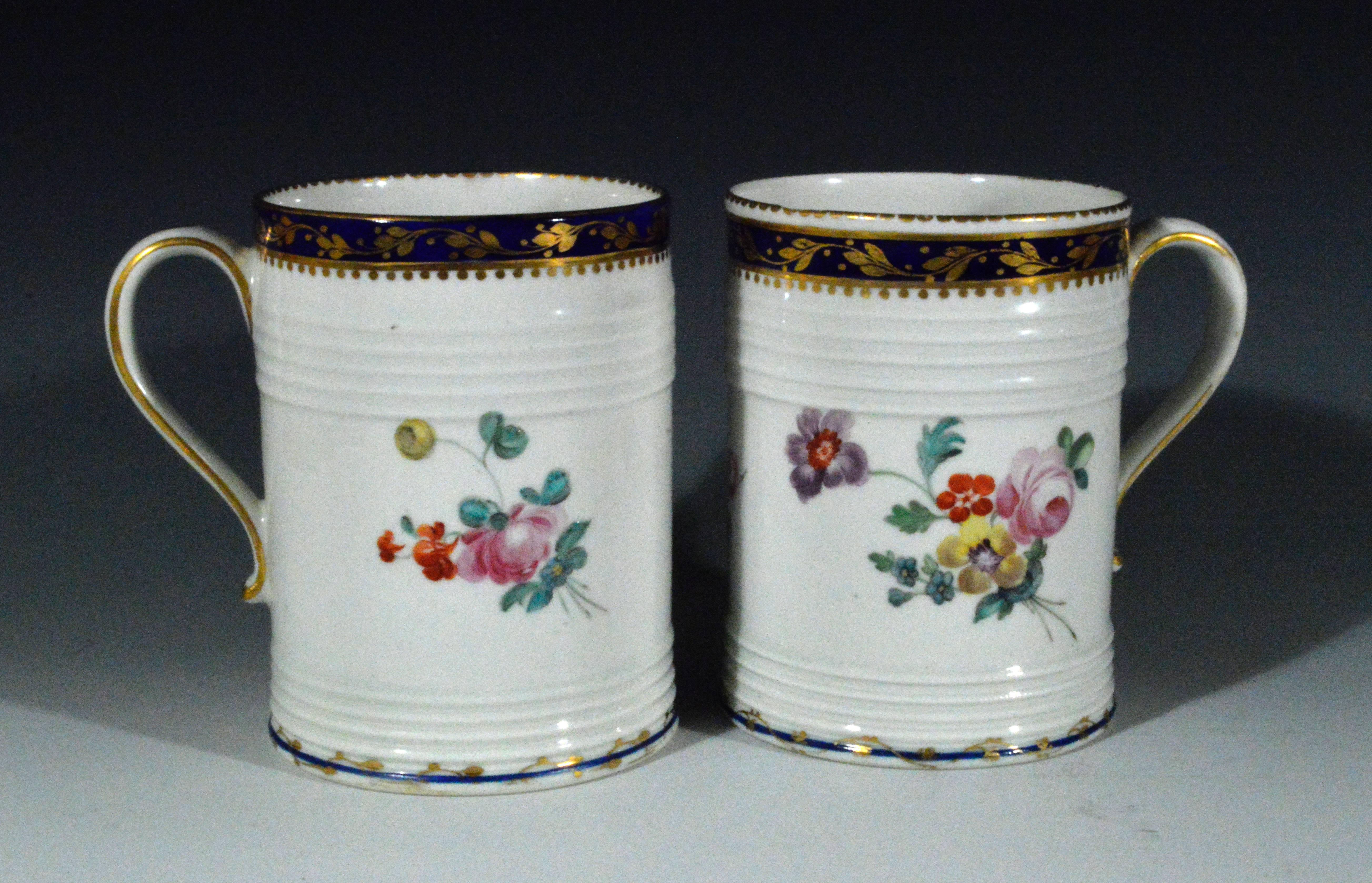 The pair of 18th century Derby porcelain botanical tankards with painted botanical decoration of flower bouquets to each side and a single flower to the front. The rim with a band of a dark blue ground with a continuous gilt leaf meandering