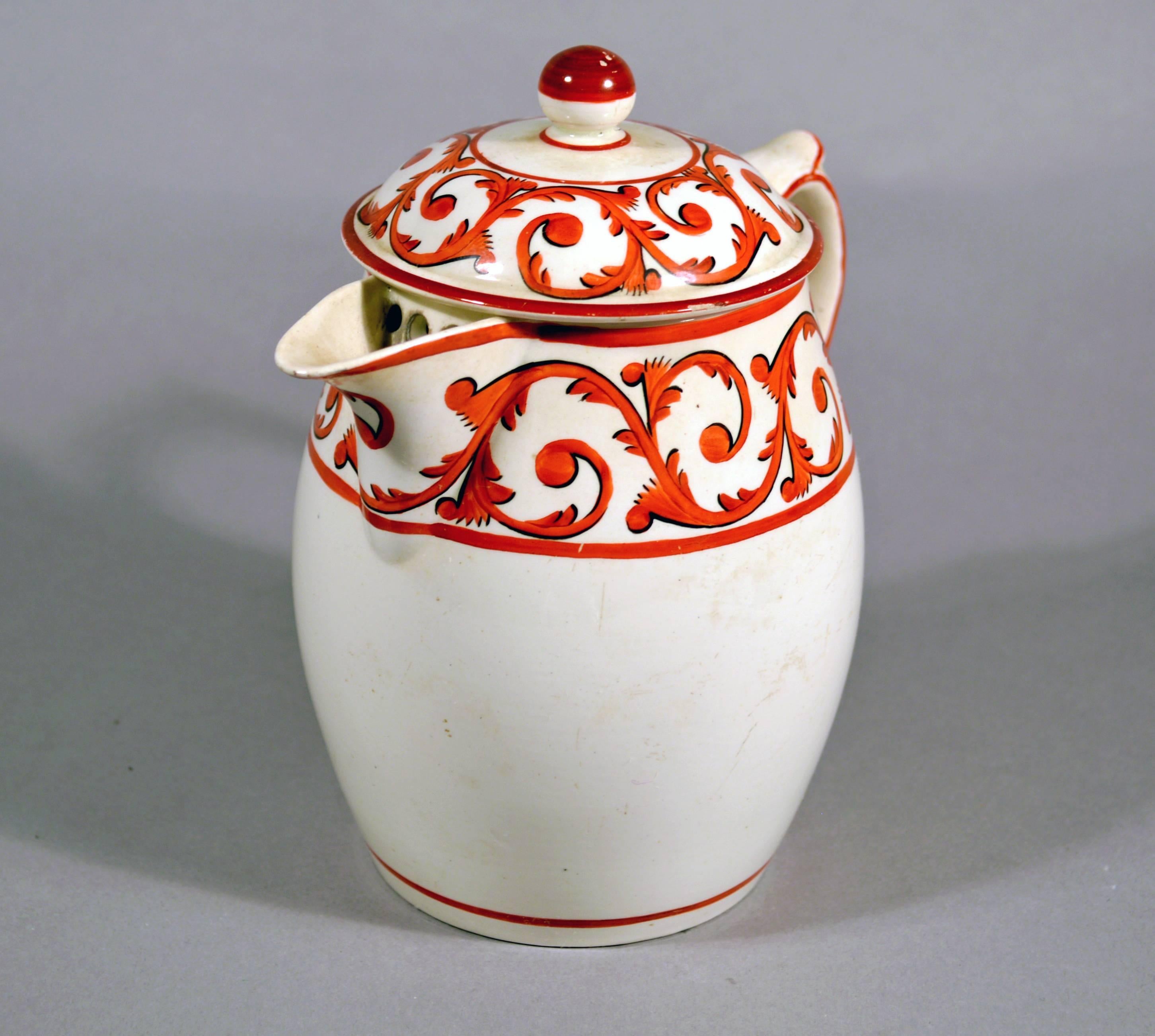 Pottery covered jug and cover with orange foliate scroll designs,
circa 1820.

The covered  jug and cover with scrolling foliate decoration in orange with black outline. The interior with pierced drainage holes at the spout and the cover with