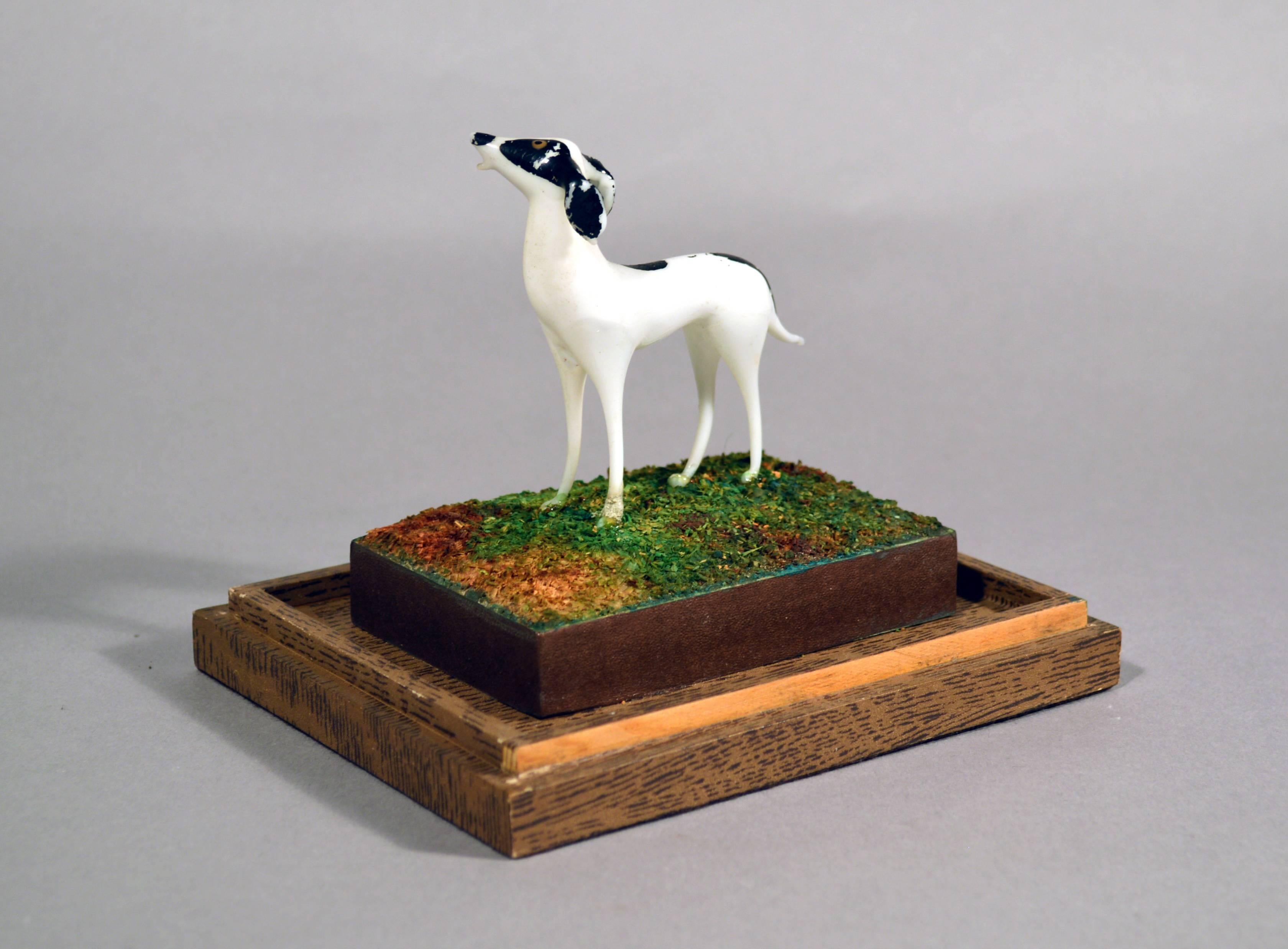 The vintage Lauscha glass shadow box with glass dog was made in Germany in the 1930s.

The white glass dog with black painted spots is depicted in a landscape created by a papered ground and backdrop standing on a raised mould depicting grass