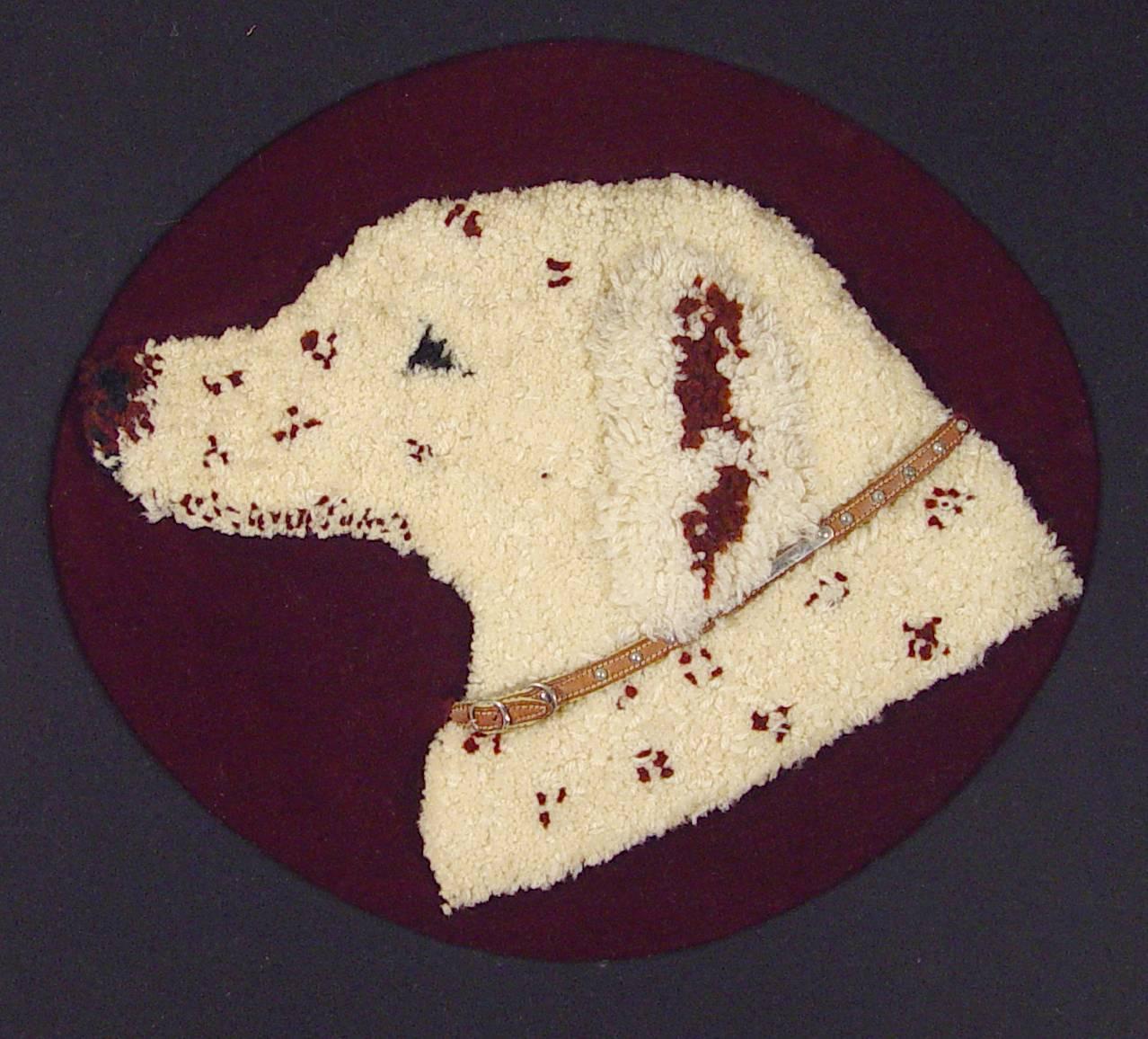 The large stumpwork picture of a dog's head with a leather collar mounted on a red felt ground with a black oval mat within a gilt and black frame.