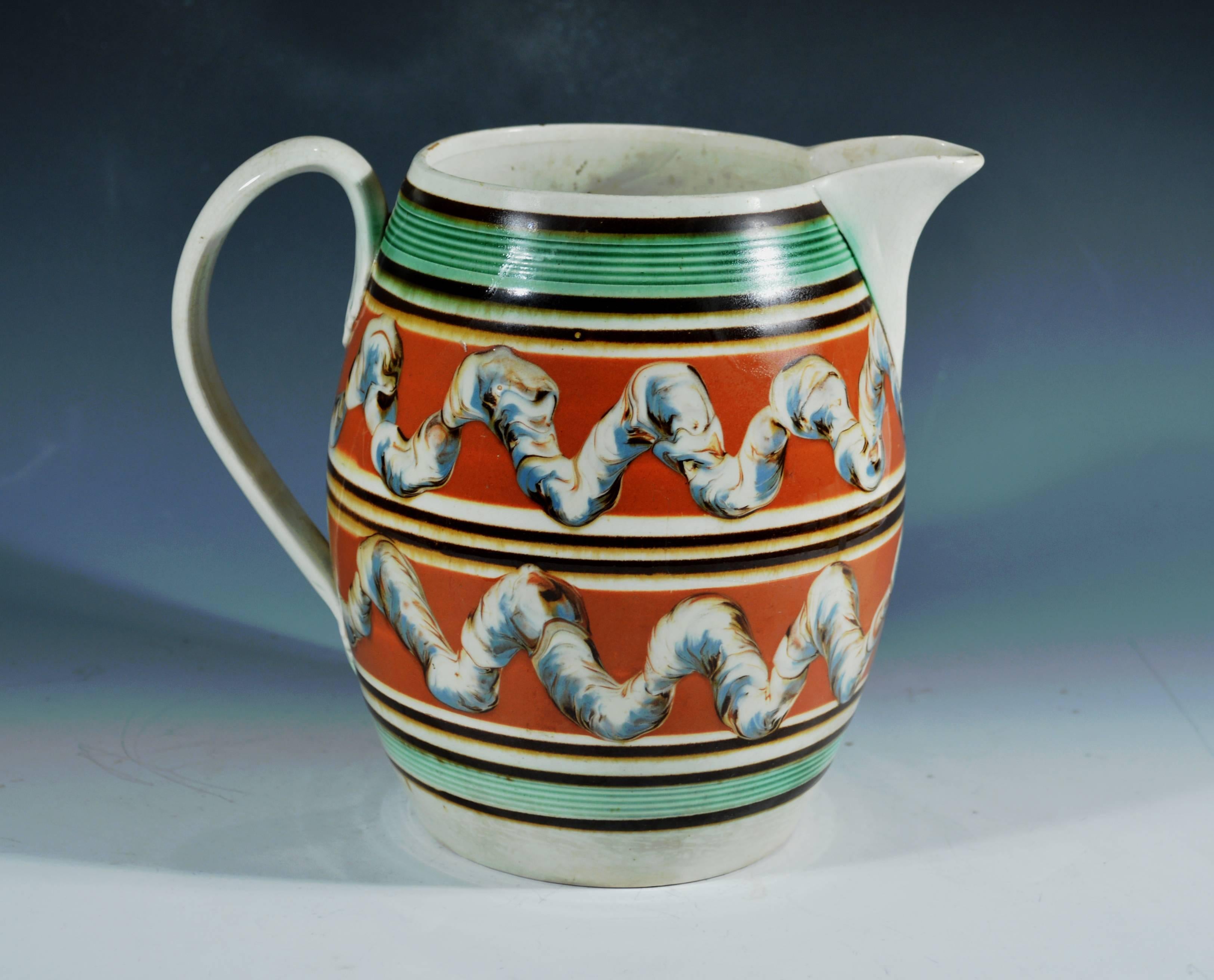 Creamware double earthworm mocha jug, 
circa 1800-1820.

The mocha jug with green reeded bands to top and bottom with molded multiple bands of raised lines colored brown with two large bands of an ochre-ground with an earthworm design encircling