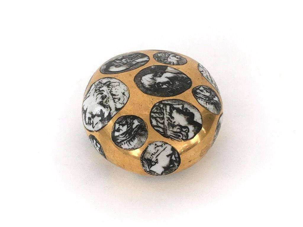 Piero Fornasetti Roman Porcelain Paperweight,
1950s.

Oval pebble-form paperweight in gold with oval panels of Roman figures.

Mark: Fornasetti Milano made in Italy.

Reference: Fornasetti: The Complete Universe, edited by Barnaba Fornasetti,