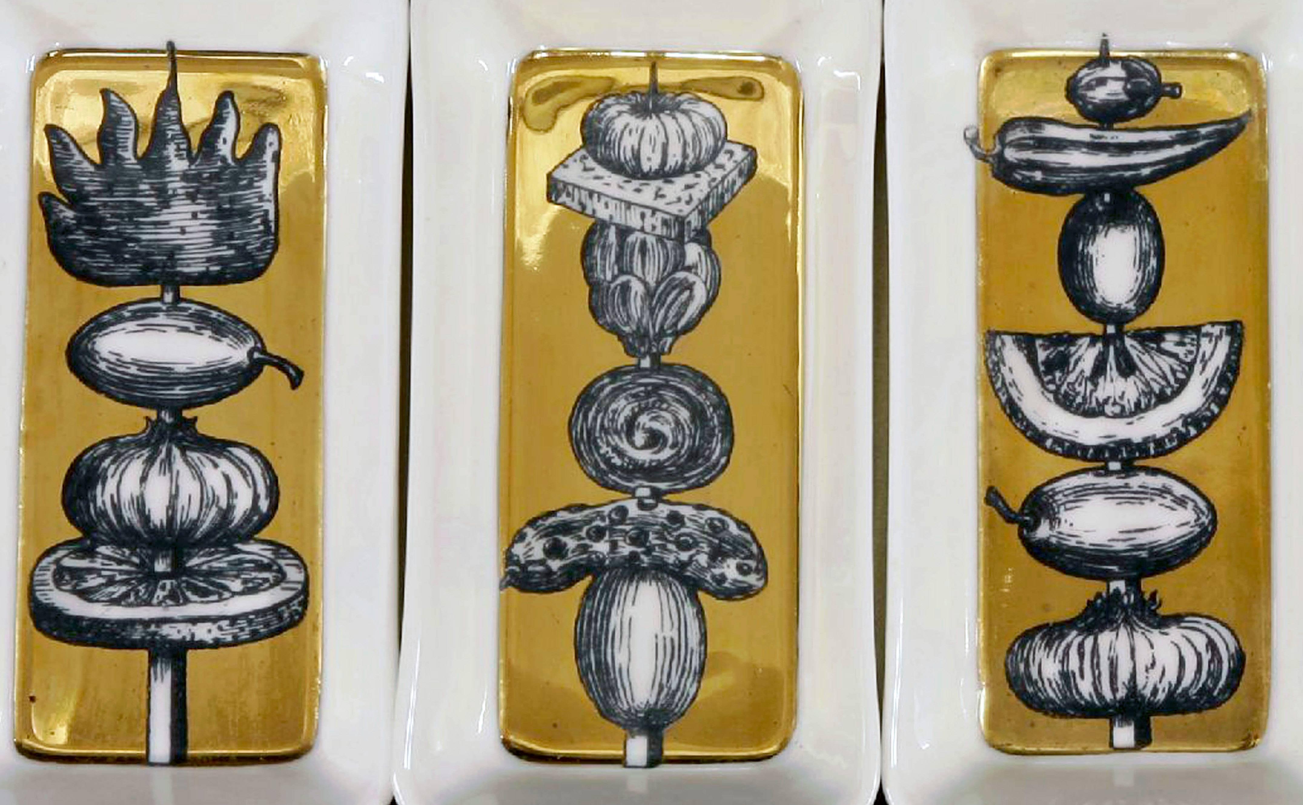 Piero Fornasetti gold 'Spiedi' appetizer dishes on original tray,
Spiedi (skewers) pattern,
early 1960s.

The set of six rectangular Piero Fornasetti 'Spiedi' pattern dishes are each decorated with skewered food on a gilt background sitting upon