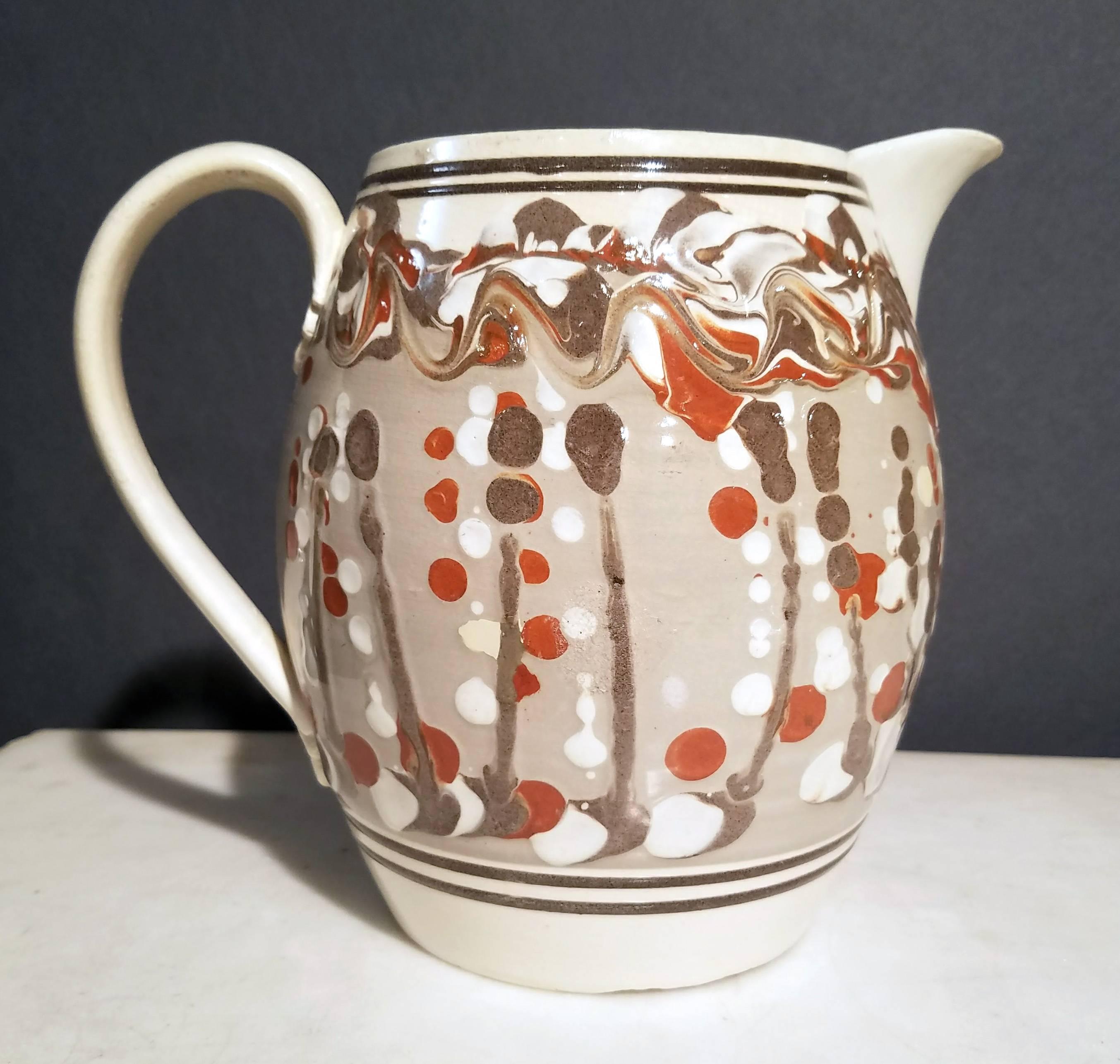 Mocha creamware large jug, 
circa 1800-1820.

A creamware jug unusually decorated with a very individualistically decorated jug with a central band of gray ground with lines and drops in red, white and dark gray.

 