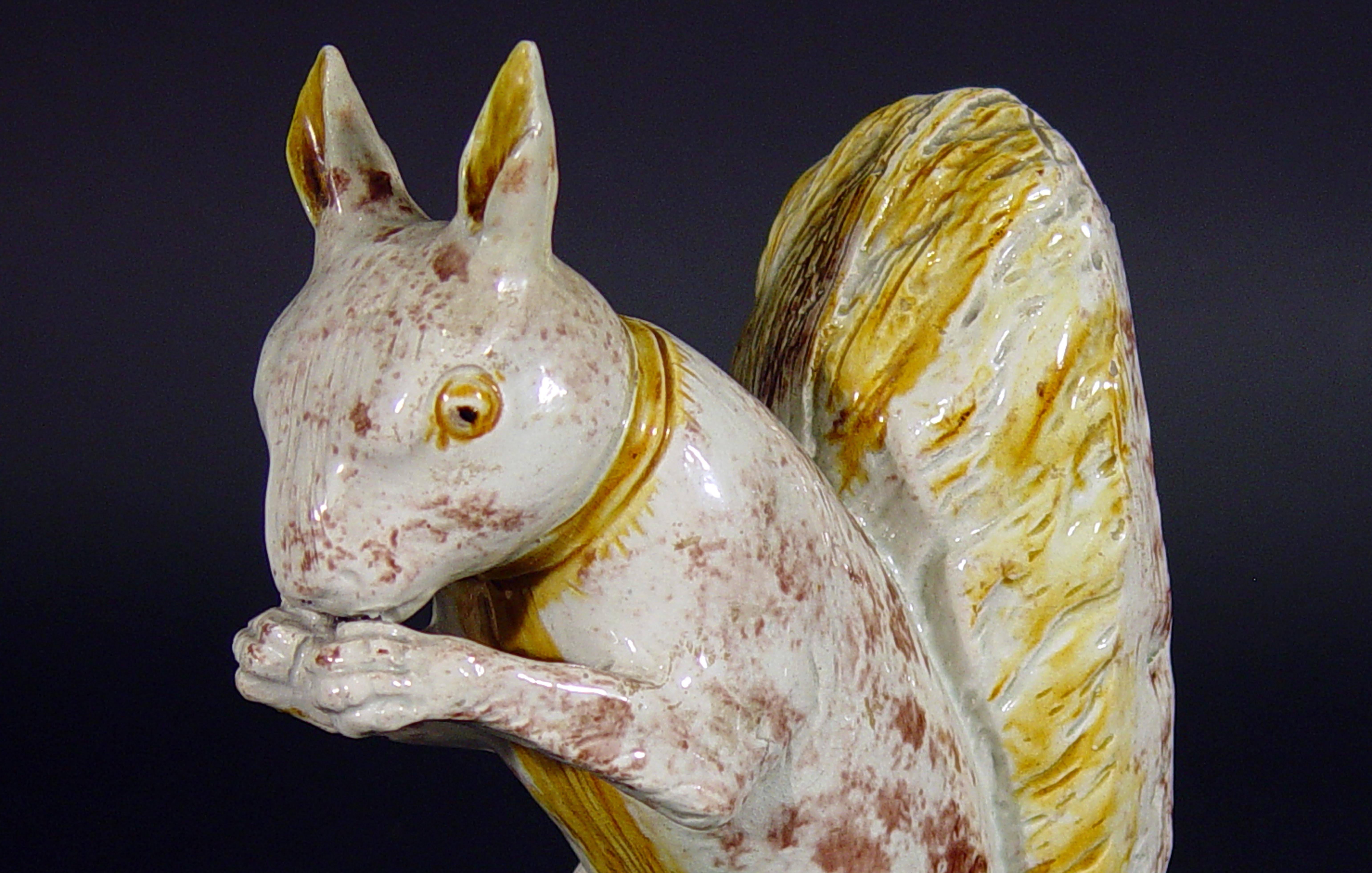 Rare early creamware model of a squirrel, 
Ralph Wood Type,
circa 1765-1780.

The pet squirrel is press moulded and is modelled with its paws holding a nut to its mouth. The squirrel is naturalistically coloured in a pale colour with patches of