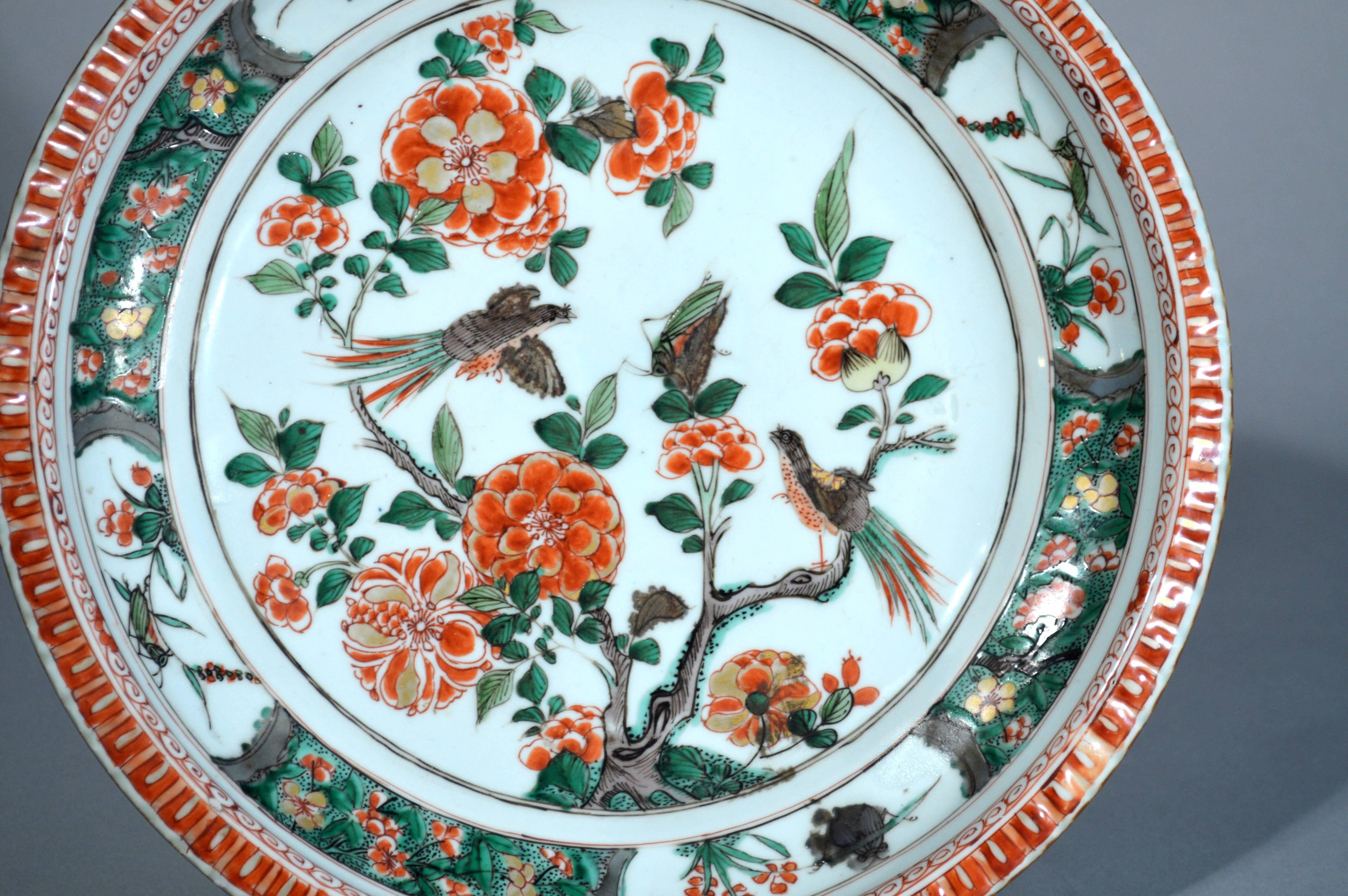 Chinese export porcelain Famille Verte dish, Kangxi period, circa 1700-1720.

The circular deep dish had a central design of a tree with iron-red blossoms with one bird alighted on a branch and another hovering, both watching a large cricket which
