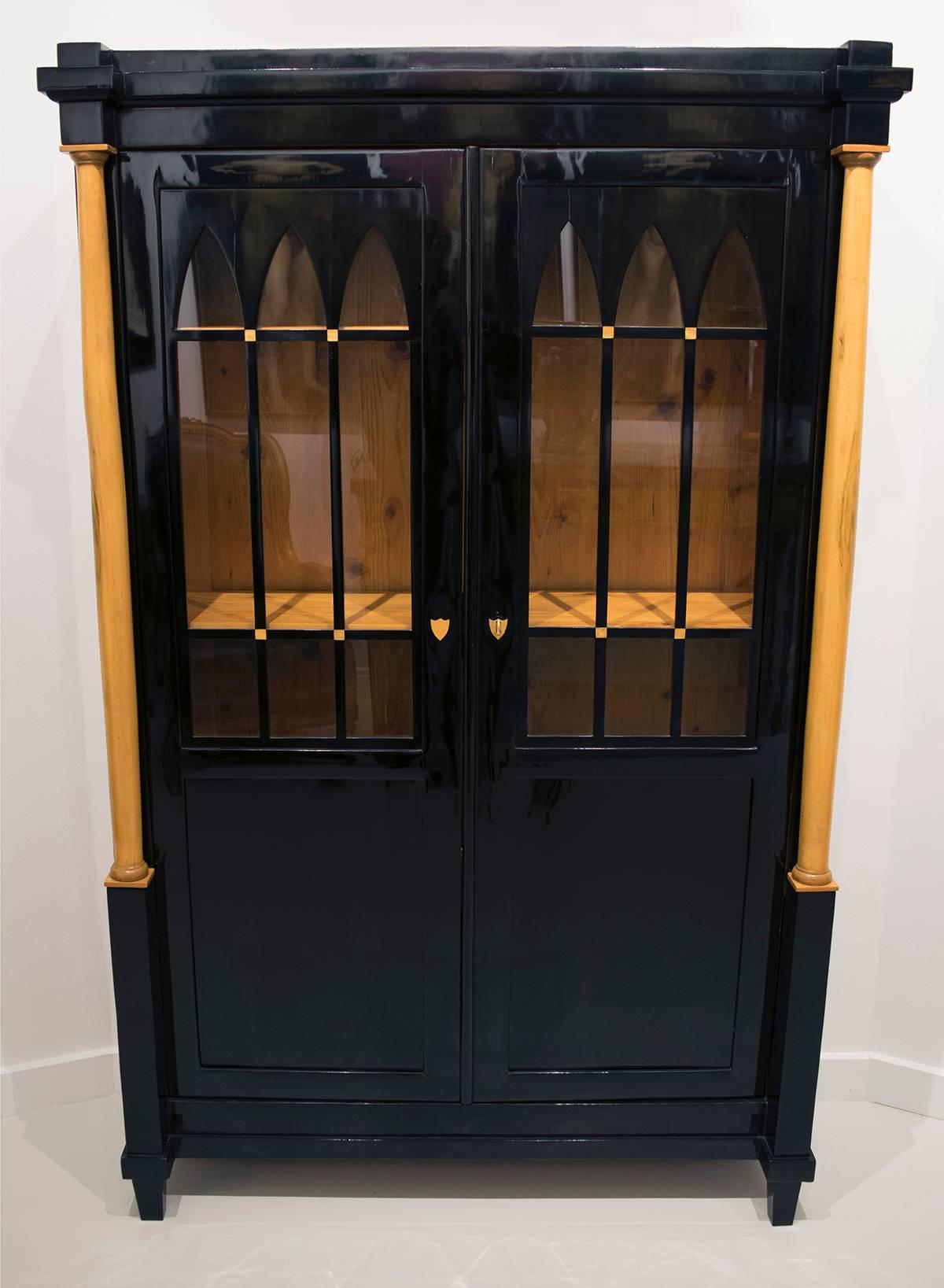 An Austrian Biedermeier ebonized wood cabinet, early 19th century. Doors feature arched glass panels; three interior shelves.