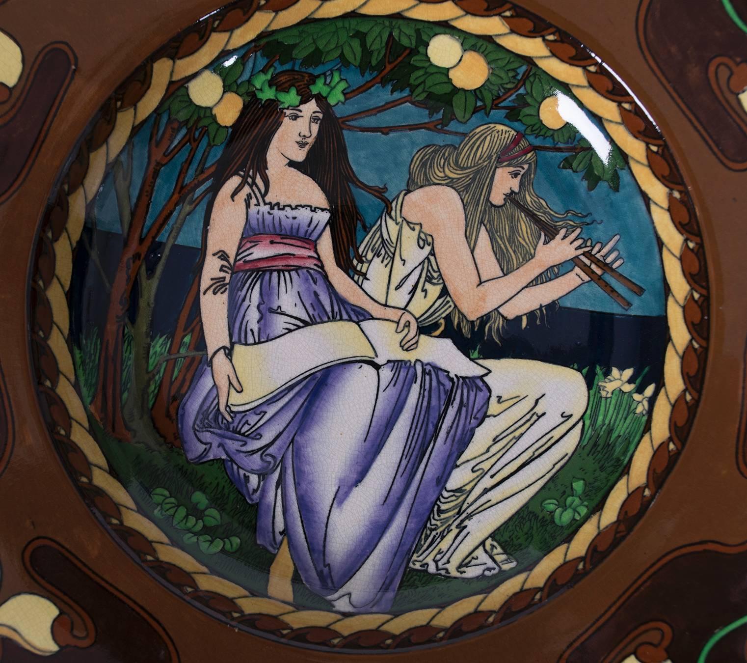 A British Art Nouveau period "Intarsio" wall plate designed by Frederick Rhead for A. Wileman & Co./Foley. Central design of two classical maidens in garden setting, within broad, richly enamelled border. Rhead (1856-1933) was the