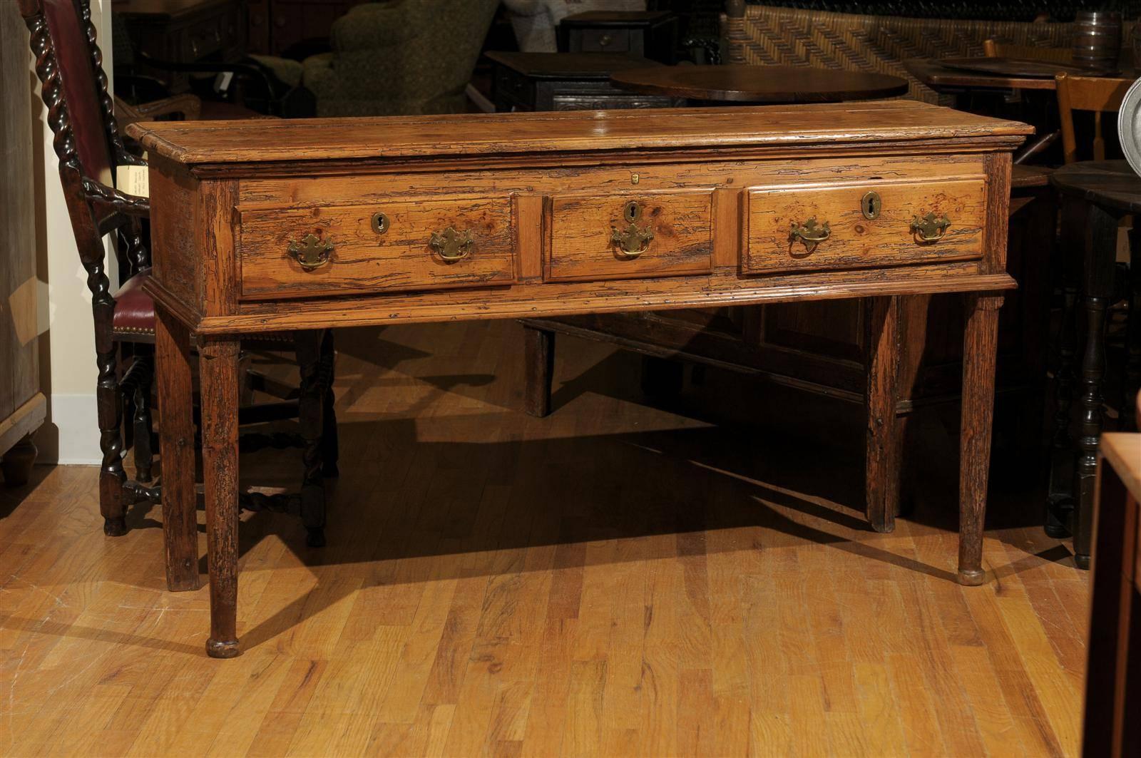 A wonderful 19th century pine server with padded legs in the front and straight legs in the back. It has a waxed finish with a lovely patina. The Chippendale pulls and escutcheons on the three drawers are brass.