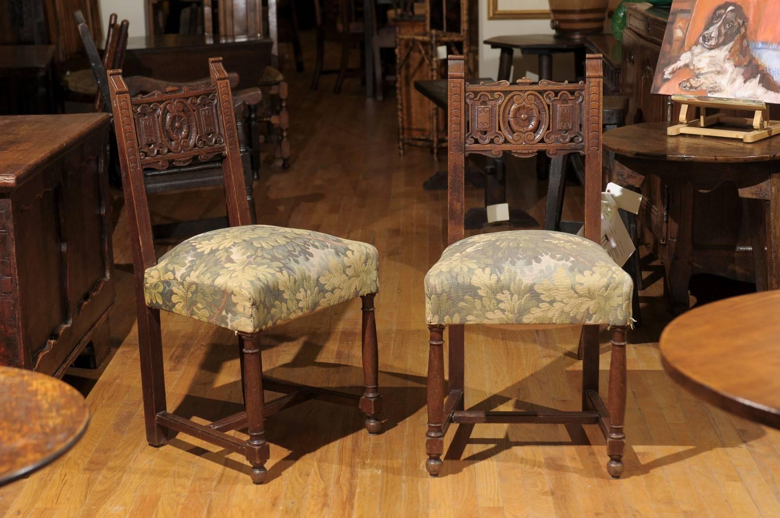 This pair of oak, upholstered chairs has backs that are hand-carved. The upholstery is a pale yellow, green and brown floral.