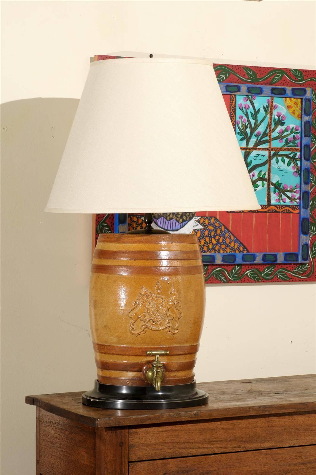 This handsome English water filter converted to a lamp is adorned with a coat of arms bearing a rampart lion and unicorn. It is in neutral tones of caramel and beige. It would add greatly to the Ambience of any room.