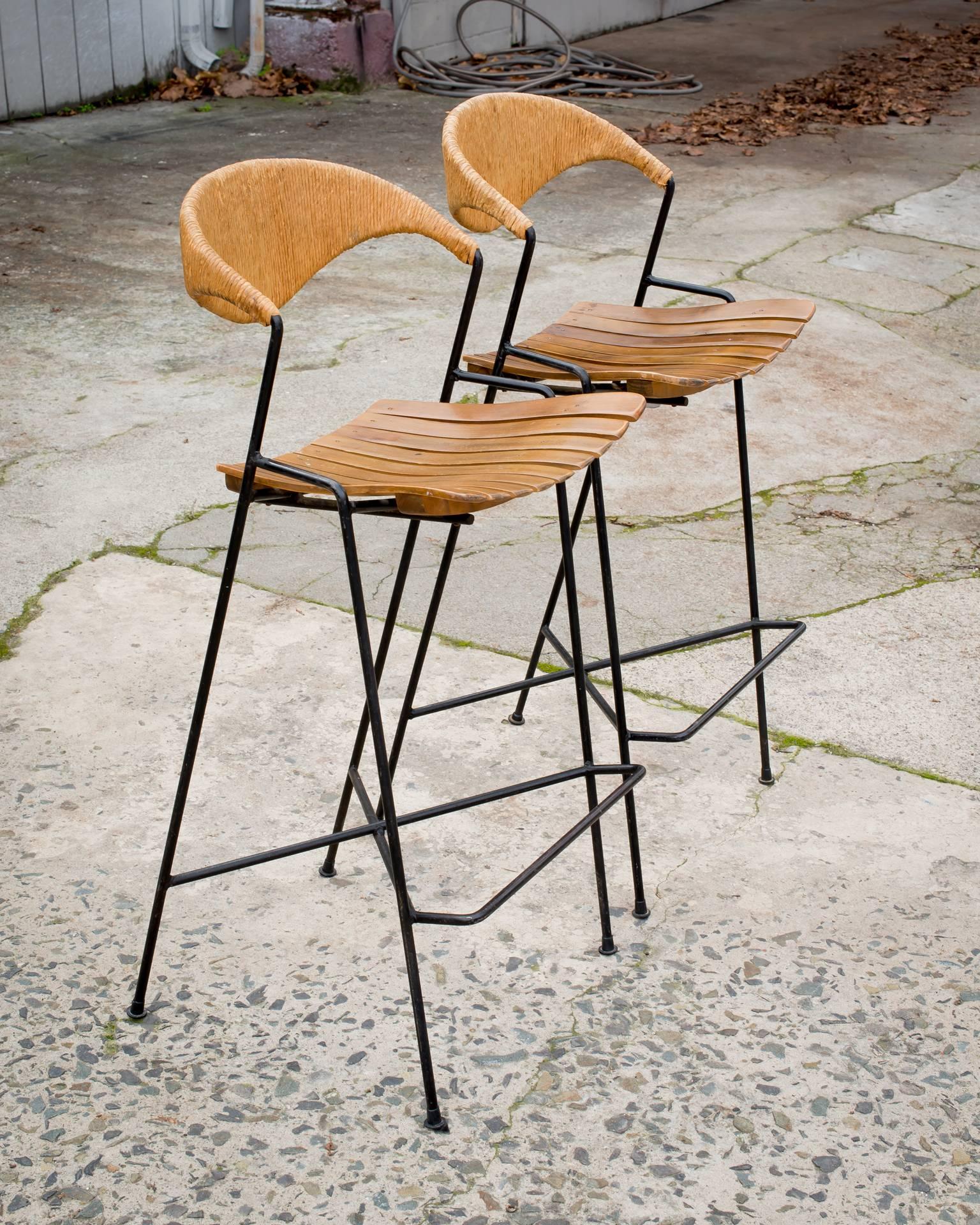 Iconic Pacifica Stools built with Umanoff’s signature materials. 
Pair of all-original Mid-century Umanoff Barstools in exceptional condition. 
Distributed by Raymor. Curved wood seat, seagrass wrapped free-form backs and super-sturdy rod-iron