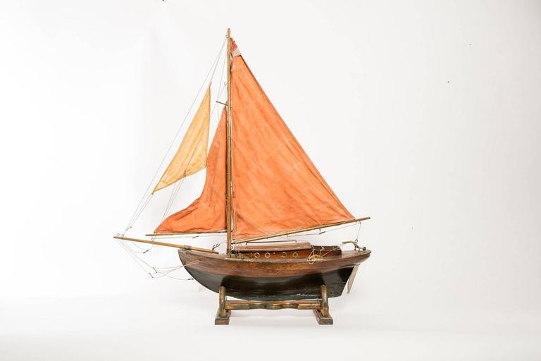 Model ship with a brown and black body and red sails, circa 1920.