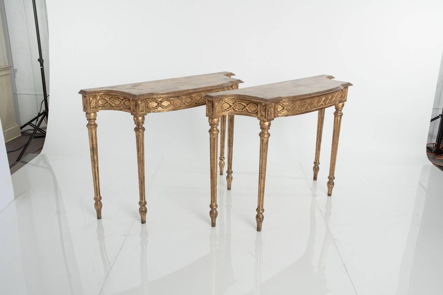 Pair of Louis XVI style gilt console tables with tapered feet and ornamented apron.