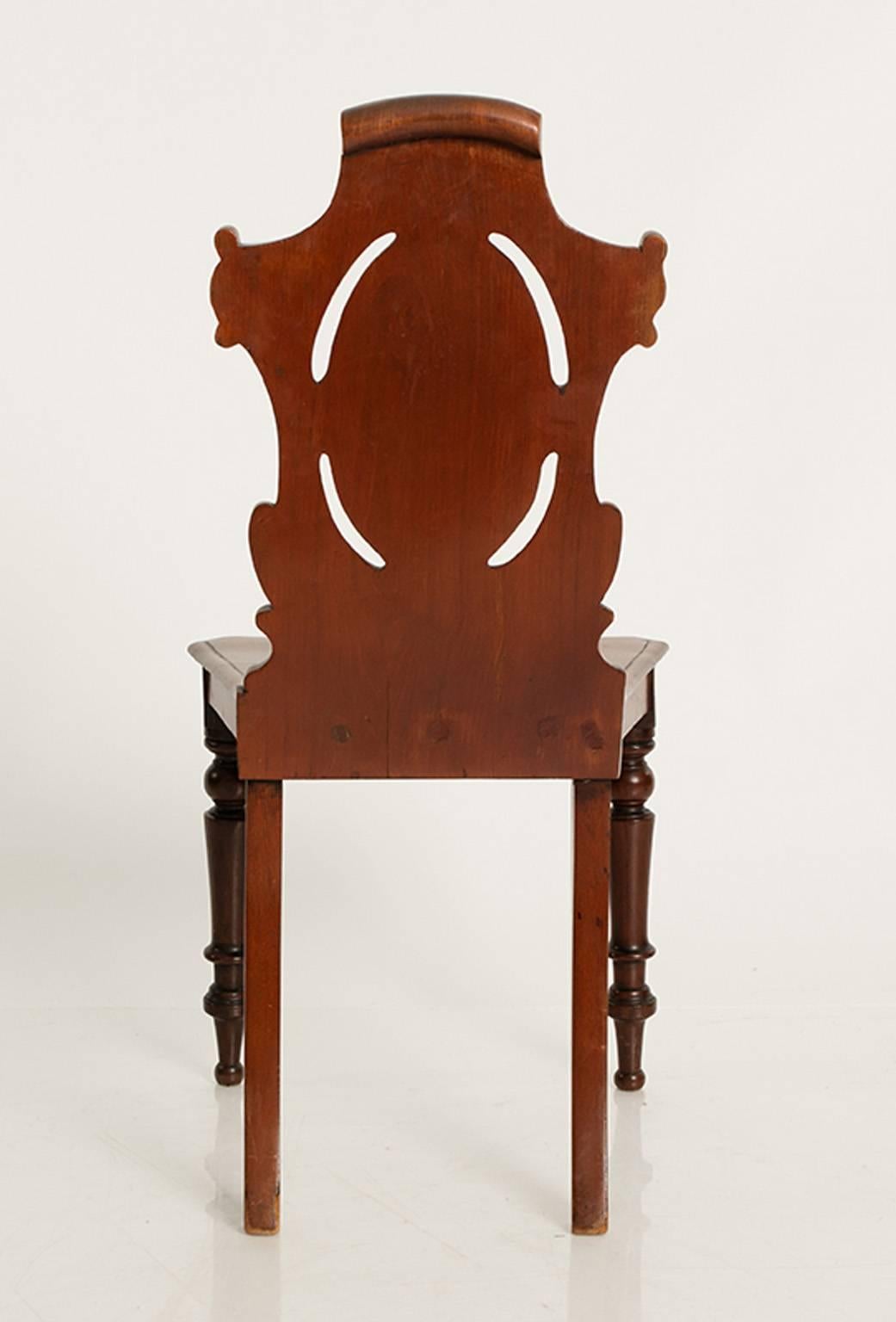 Pair of 19th century hall chairs with carved backs, turned legs, and a plank seat. 