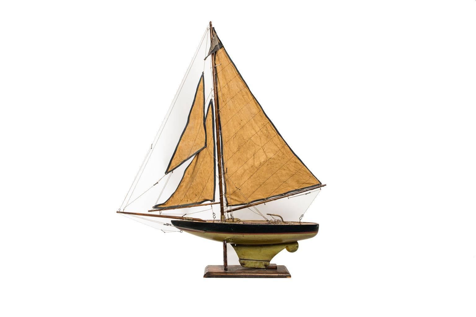 Model ship with a brown body and green sails, circa 1920.