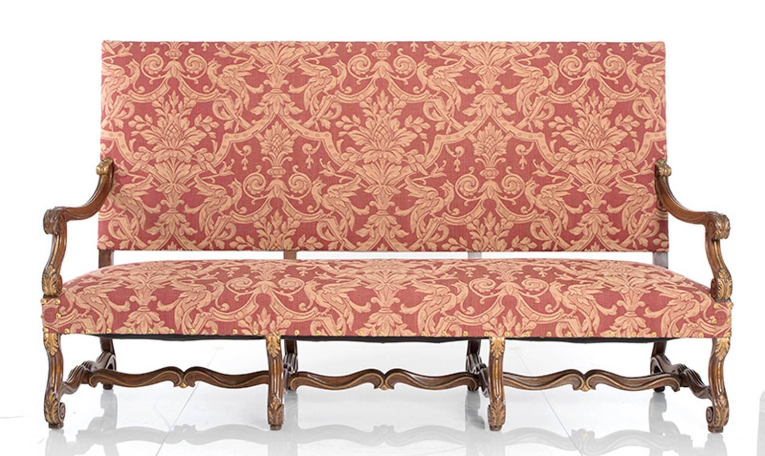 20th century Jacobean style settee. There are eight legs, elements of which are gilded. The settee is upholstered in a red and gold damask type fabric.
  