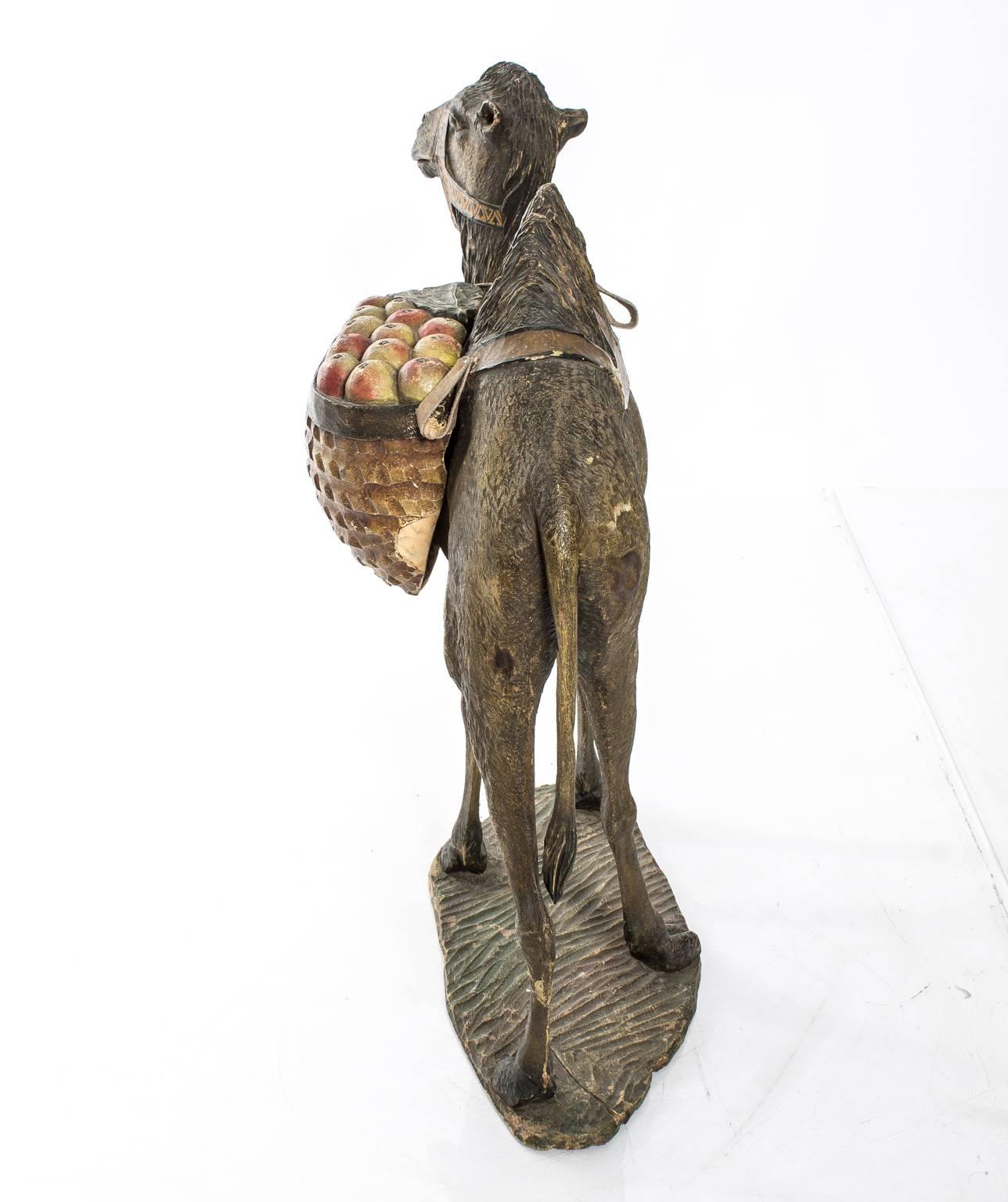 Early 20th century polychrome wooden carved camel figure carrying a fruit basket.