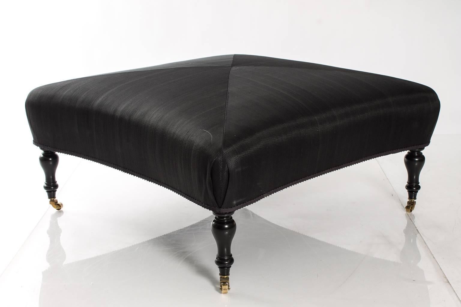Square ottoman with concave ends. Raised on ebonized turn legs and castors.