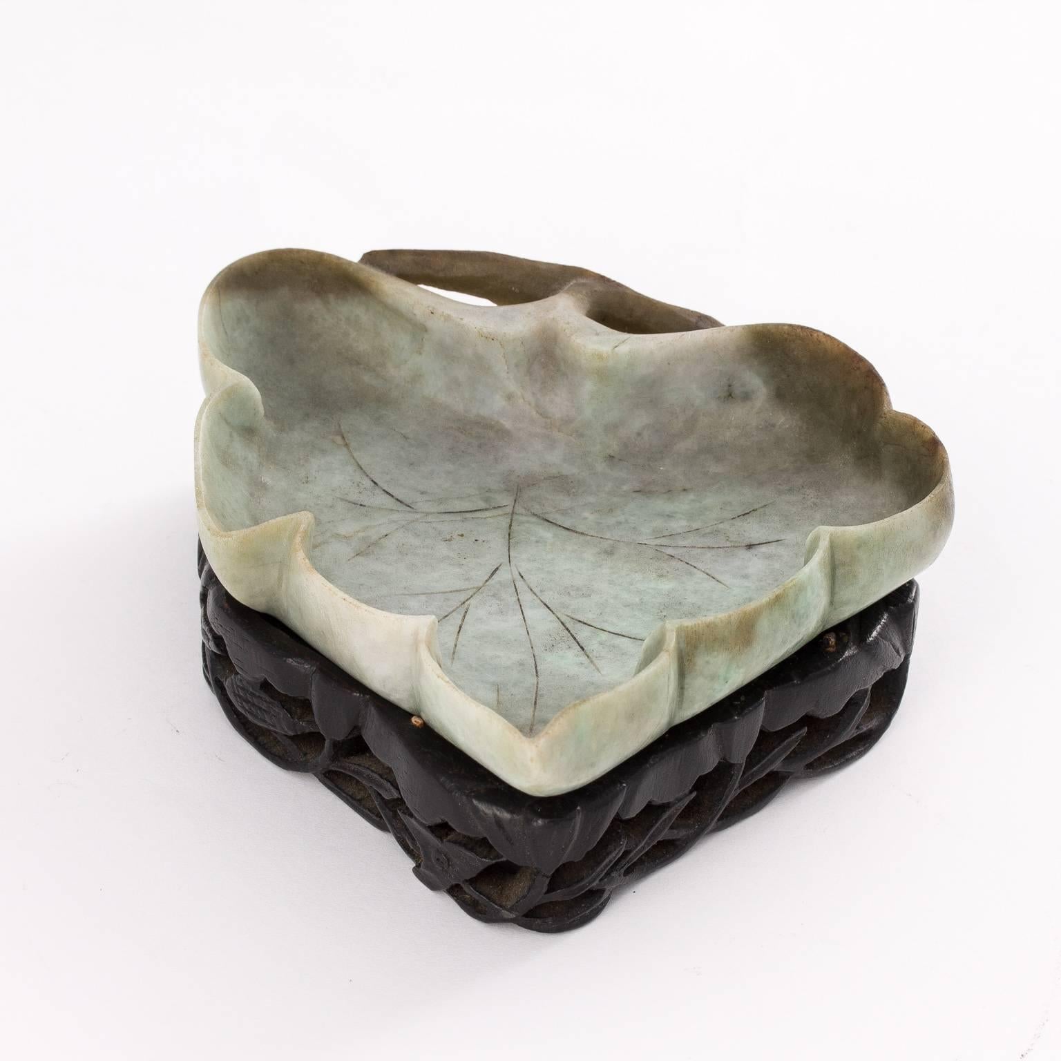 Jade inkwell stand in shape of leaf on matching carved wooden stand.