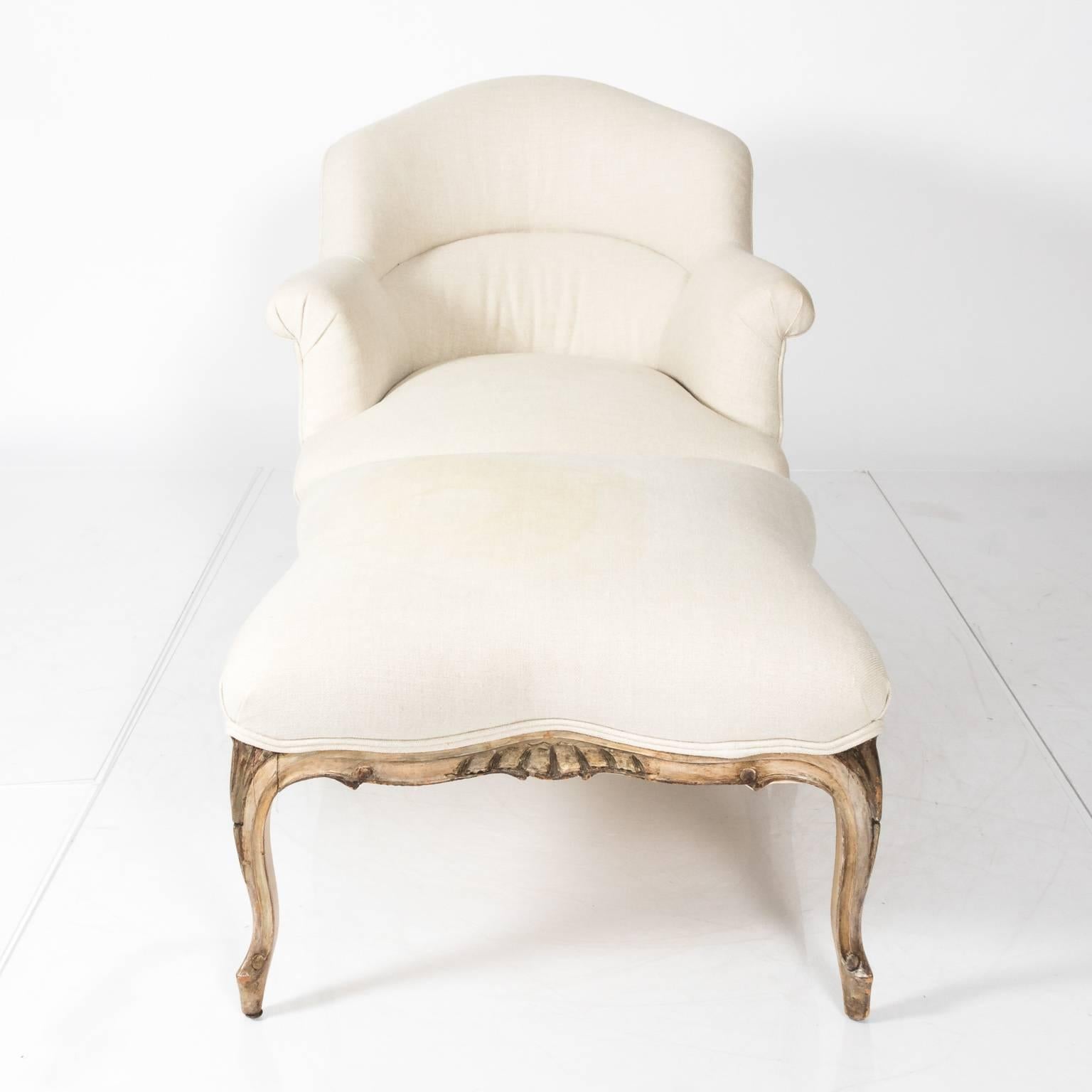 Louis XV style upholstered chair and ottoman featuring a wood frame and cabriole legs, circa 1930. There is a light stain on the upholstery of the ottoman.