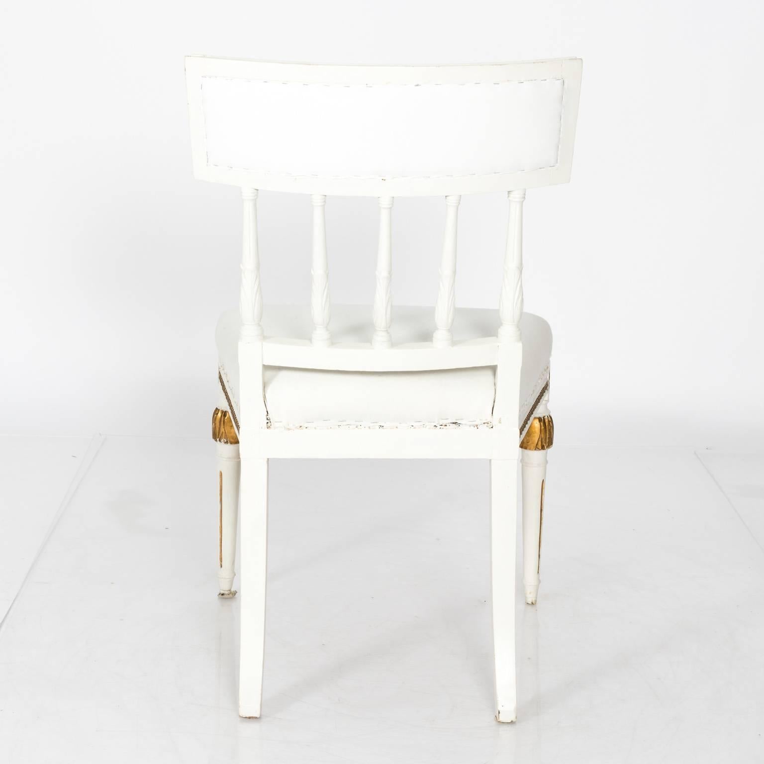 A pair of white-painted Gustavian chairs with gilt detailing, rosettes, fluted legs, circa 1800s.